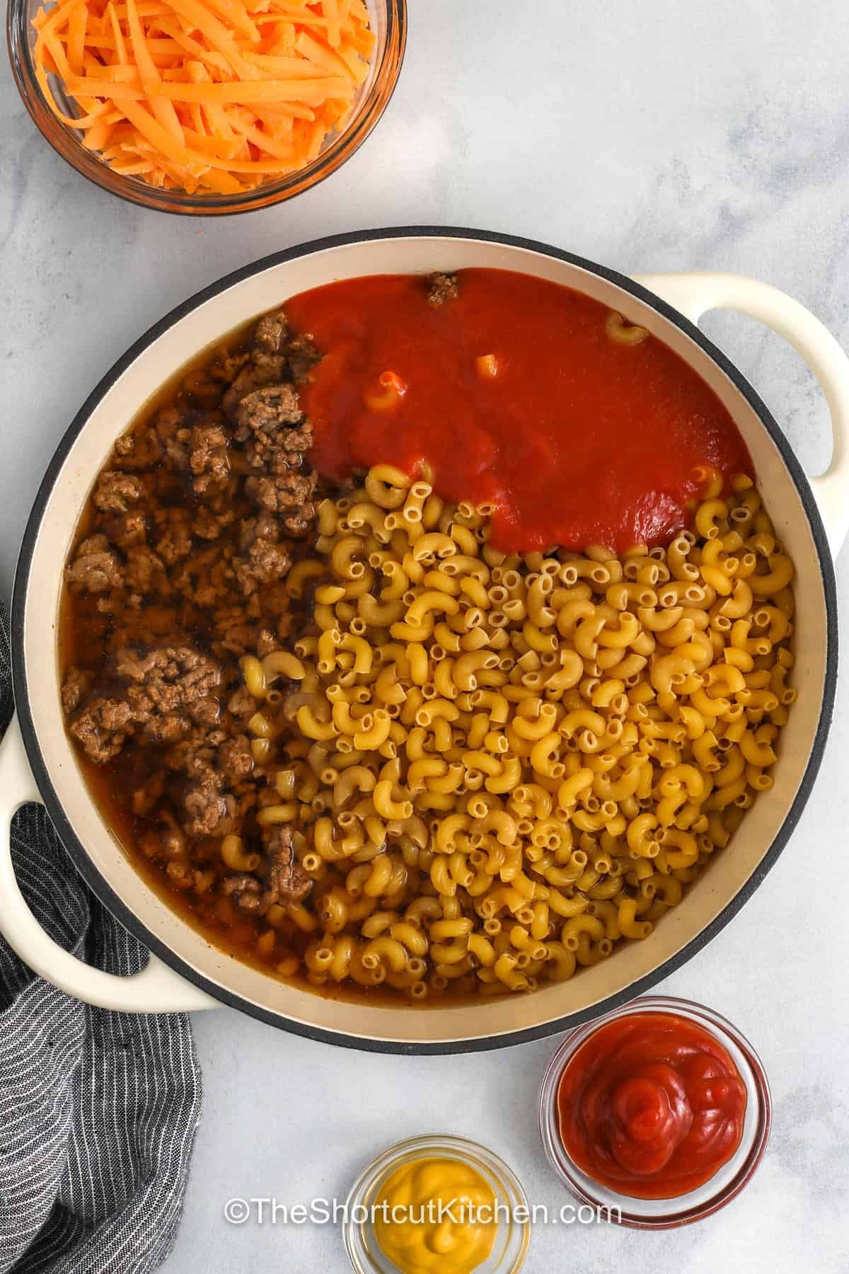 This creamy Cheeseburger Pasta is made with lean ground beef, elbow macaroni, cheddar cheese, ketchup, and yellow mustard. It has all the cozy flavor of a classic cheeseburger combined in a one-pot pasta recipe. This cheeseburger pasta is a family-friendly recipe that is filling and easy to make. It’s the perfect weeknight meal for busy nights. So save this recipe for the next time you need a simple weeknight dinner! #theshortcutkitchen adding tomato sauce , and macaroni to broth and cooked beef to make One Pot CheeseBurger Pasta