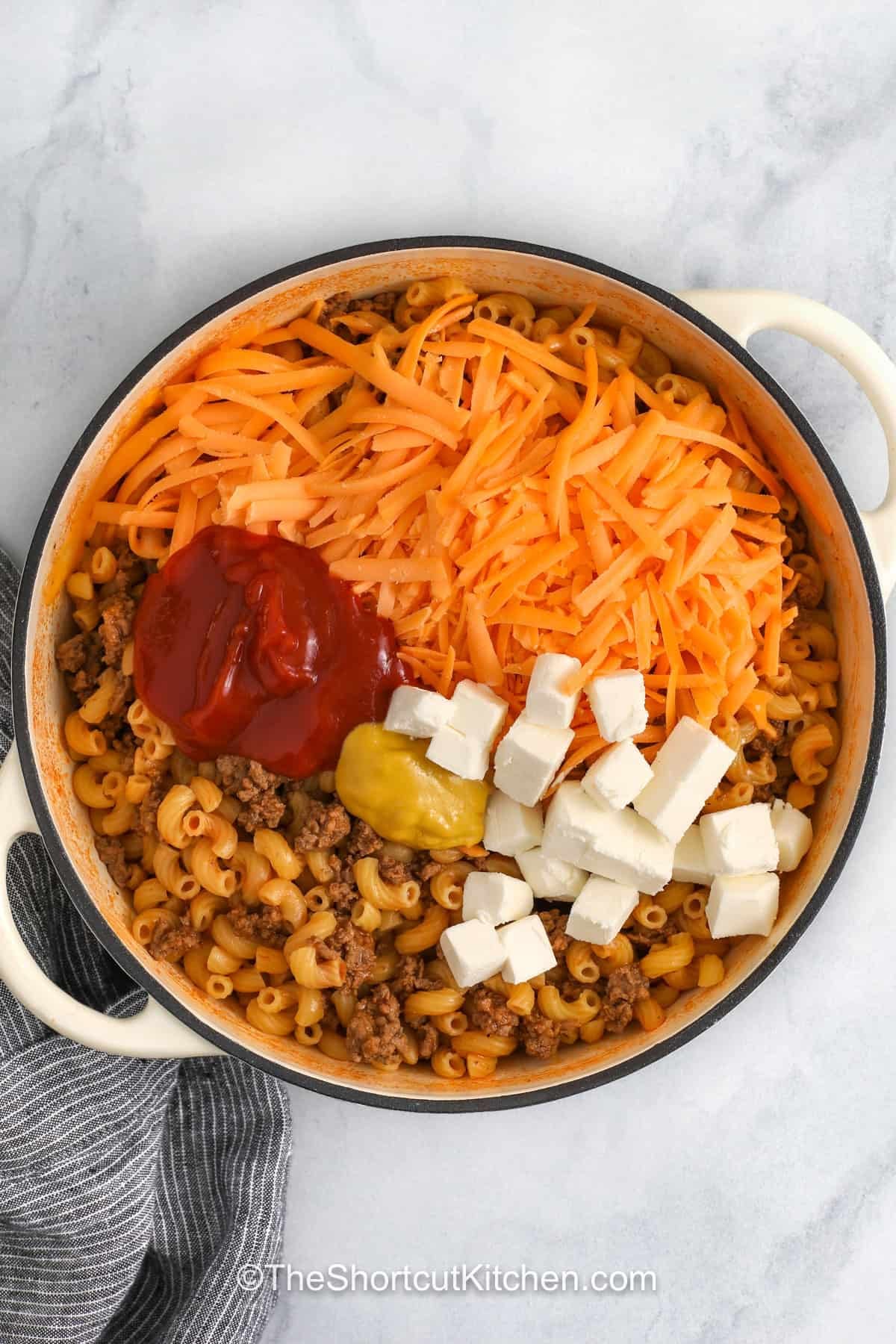 This one-pot cheeseburger pasta recipe is made with seasoned ground beef, elbow macaroni, shredded cheddar, ketchup, and mustard. It is a shortcut dinner with classic cheeseburger flavor and a creamy sauce that coats every bite. Serve it with salad, veggies, or your favorite burger toppings like pickles, bacon, or green onions. Pin it now to add it to your weeknight rotation. #theshortcutkitchen adding cream cheese , cheese , ketchup and mustard to macaroni and beef to make One Pot CheeseBurger Pasta