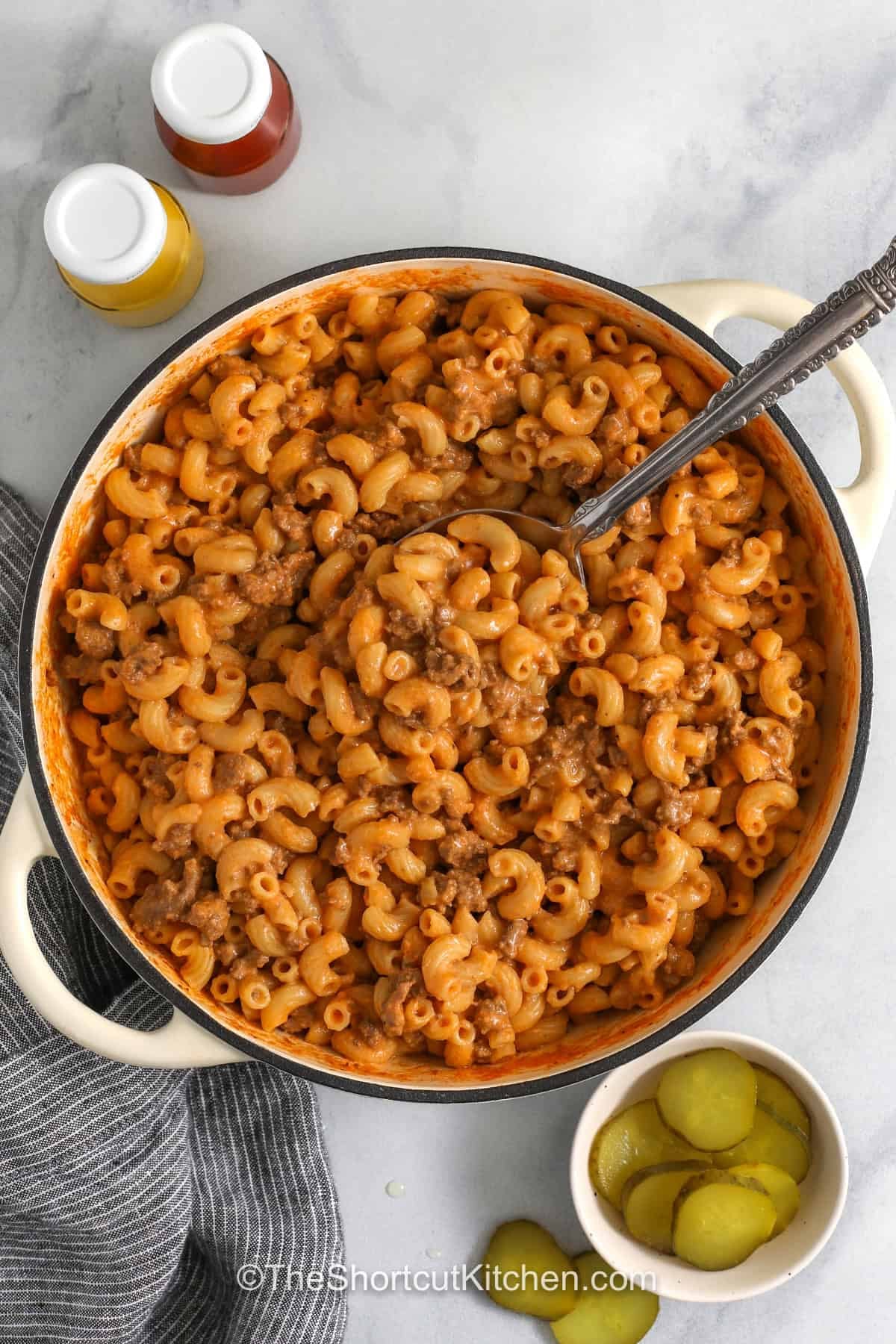 This easy Cheeseburger Pasta brings together ground beef, elbow macaroni, cheddar, cream cheese, ketchup, and mustard in one cozy skillet. It is a simple stovetop recipe with a creamy texture and big burger flavor. Ready in under 30 minutes, this cheesy pasta is a great dinner idea for busy weeknights, meal prep, or leftovers. So don’t forget to pin it today, and add it to your weekly rotation. #theshortcutkitchen creamy One Pot CheeseBurger Pasta in the pot with a spoon