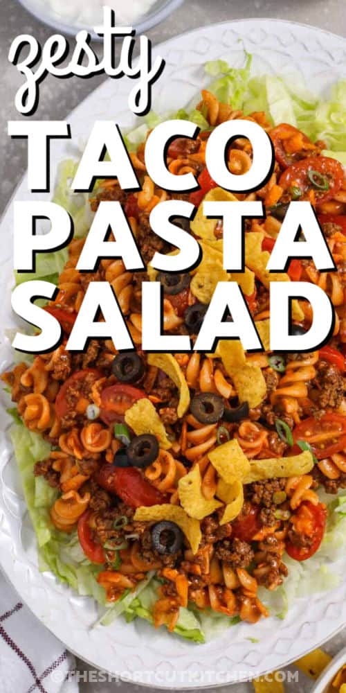 This cold taco pasta salad with ground beef is loaded with shortcut ingredients and big taco flavor. Rotini pasta, taco seasoning, shredded cheddar, cherry tomatoes, Catalina dressing, and crisp lettuce come together in a colorful salad that feeds a crowd. Keep the chips separate until serving so every bite has fresh crunch and creamy tangy dressing. Serve it at the next potluck, or for a quick dinner. #theshortcutkitchen zesty Taco Pasta Salad with writing