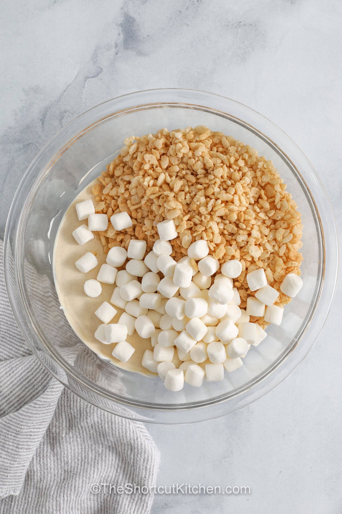 Perfect for quick desserts, avalanche cookies are a no-bake treat filled with peanut butter, white chocolate, marshmallows, and crisp rice cereal. The combination creates a chewy and crunchy cookie that everyone enjoys. They are great for parties, gifting, or keeping on hand for sweet cravings. Simple ingredients make them easy to prepare and fun to share. Try this recipe and make dessert time extra special. #theshortcutkitchen adding ingredients to bowl to make Avalanche Cookies