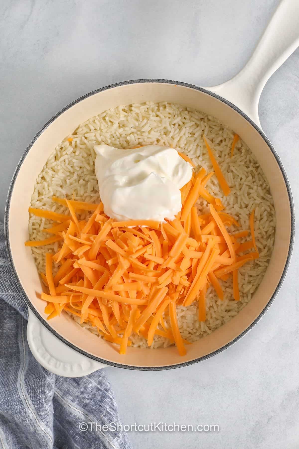 For weeknight meals, cheesy rice is always welcome at the table. This creamy rice recipe uses pantry staples, and cheddar brings plenty of flavor to every bite. Serve it with baked chicken, roast beef, or pork tenderloin for an easy family dinner. It is a comforting side dish that works for holidays and everyday meals alike. Everyone will be asking for seconds when this recipe is served. Try this cheesy rice recipe today. #theshortcutkitchen adding cheese and sour cream to rice to make Cheesy Rice