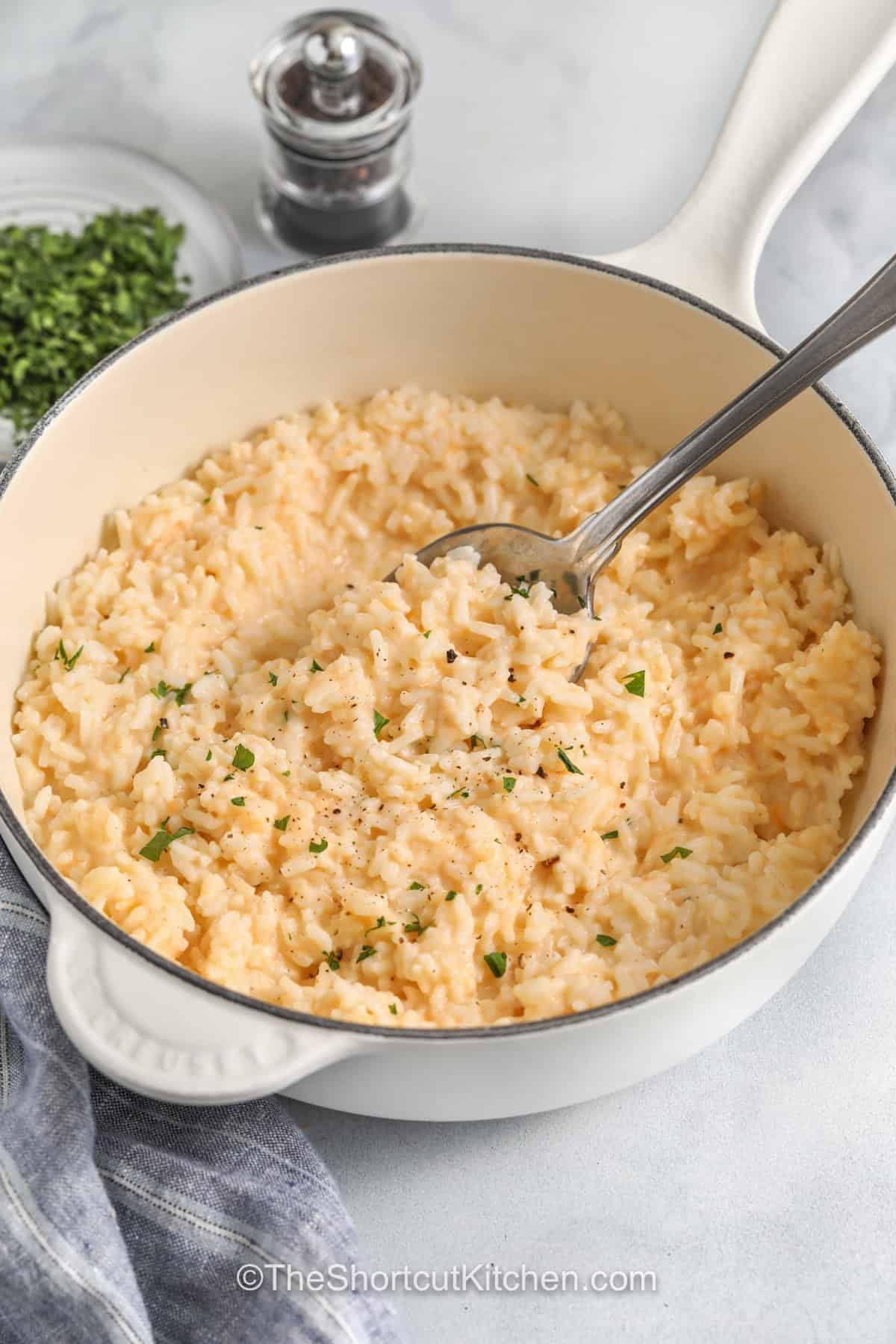Cheesy rice belongs on the menu when you want an easy and comforting side. This homemade recipe is creamy, flavorful, and made with simple pantry staples. It complements chicken, beef, and pork dishes with plenty of cheesy goodness in every bite. Families love how versatile and satisfying this classic recipe can be. It is perfect for everyday dinners and special occasions. Save this recipe and make it for your family soon. #theshortcutkitchen pot of Cheesy Rice with a spoon