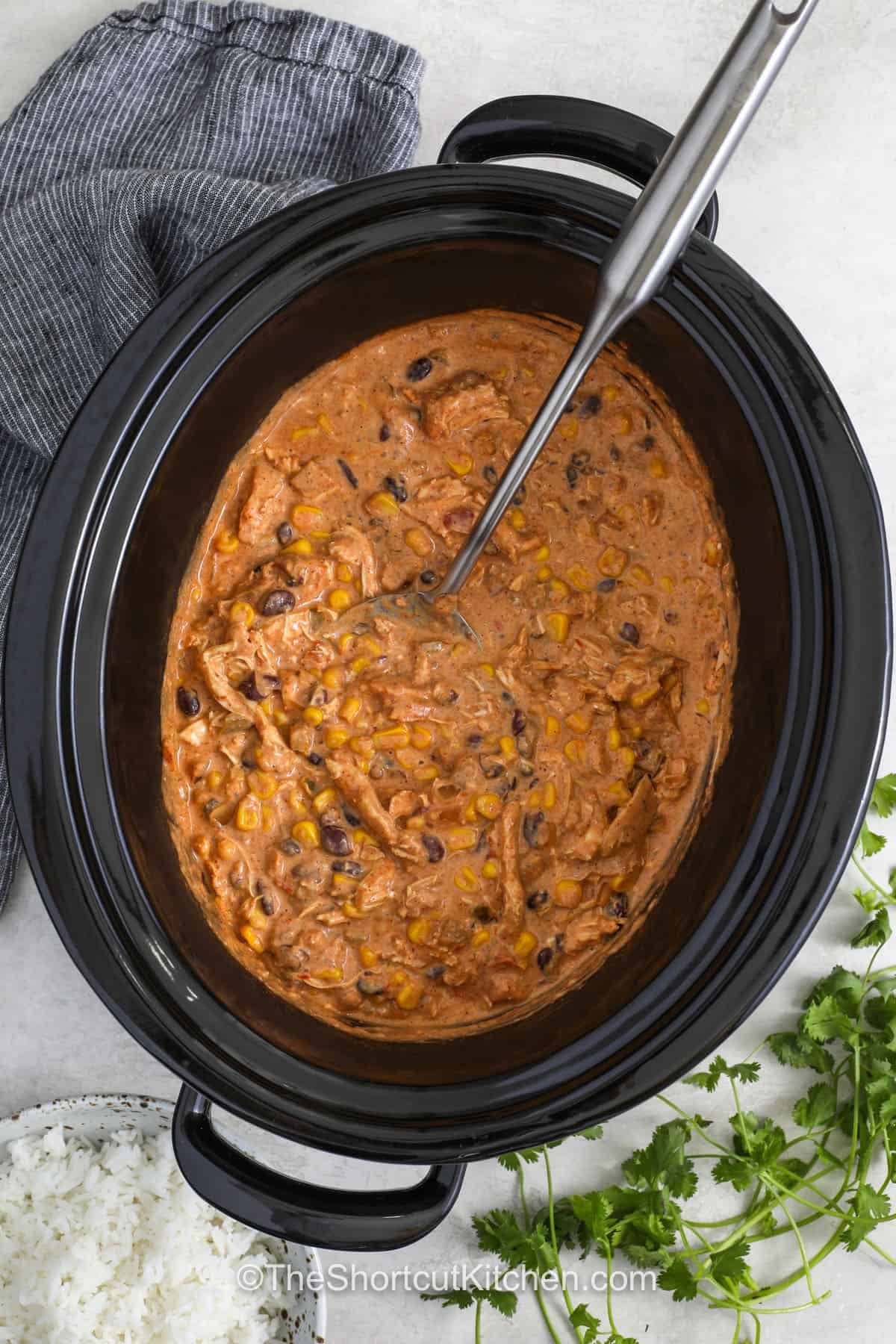 This fiesta chicken recipe is the easy dinner your family will ask for again and again. Tender shredded chicken cooks with salsa, taco seasoning, black beans, and corn for bold Tex-Mex flavor. Cream cheese is stirred in at the end to make every bite rich and creamy. Spoon it into tacos, burrito bowls, wraps, or over rice for a meal everyone can enjoy. Save this Slow Cooker Fiesta Chicken and add it to your dinner plans today. #theshortcutkitchen crockpot of Fiesta Chicken Recipe