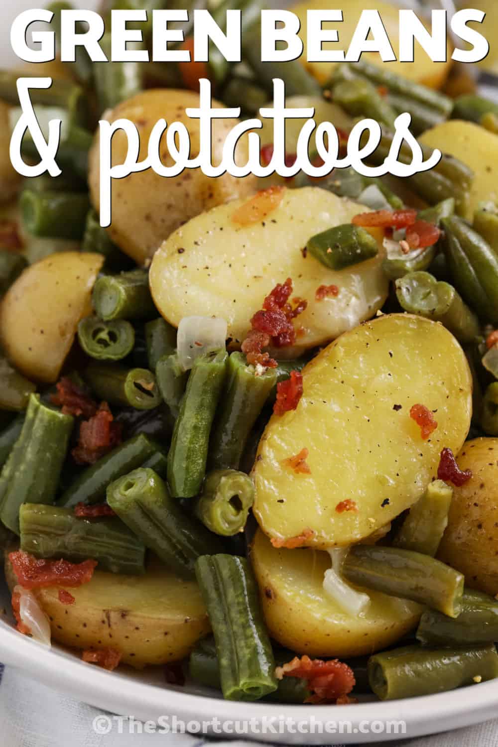 This easy green beans and potatoes side dish is perfect when you want something hearty, affordable, and comforting. Frozen green beans, halved baby potatoes, onion, chicken broth, butter, and bacon bits cook together in one skillet. It is a simple recipe with cozy flavor and very little chopping or cleanup. Pin this simple side dish to make this week! #theshortcutkitchen plated Green Beans and Potatoes with a title