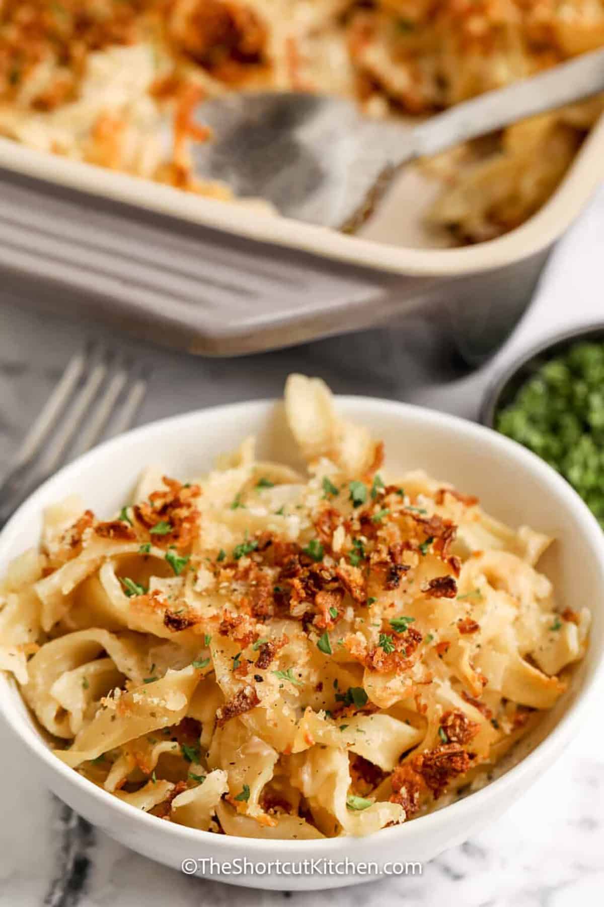 This creamy French onion casserole transforms simple egg noodles into a warm and satisfying pasta bake. The stovetop onion sauce is made with butter, beef broth, and French onion dip, while Panko, Parmesan, and crispy onions form the golden oven-baked topping. Serve French Onion Casserole as an easy meatless meal or alongside chicken, pork, or beef. Add it to your dinner board today. #theshortcutkitchen bowl of French Onion Casserole