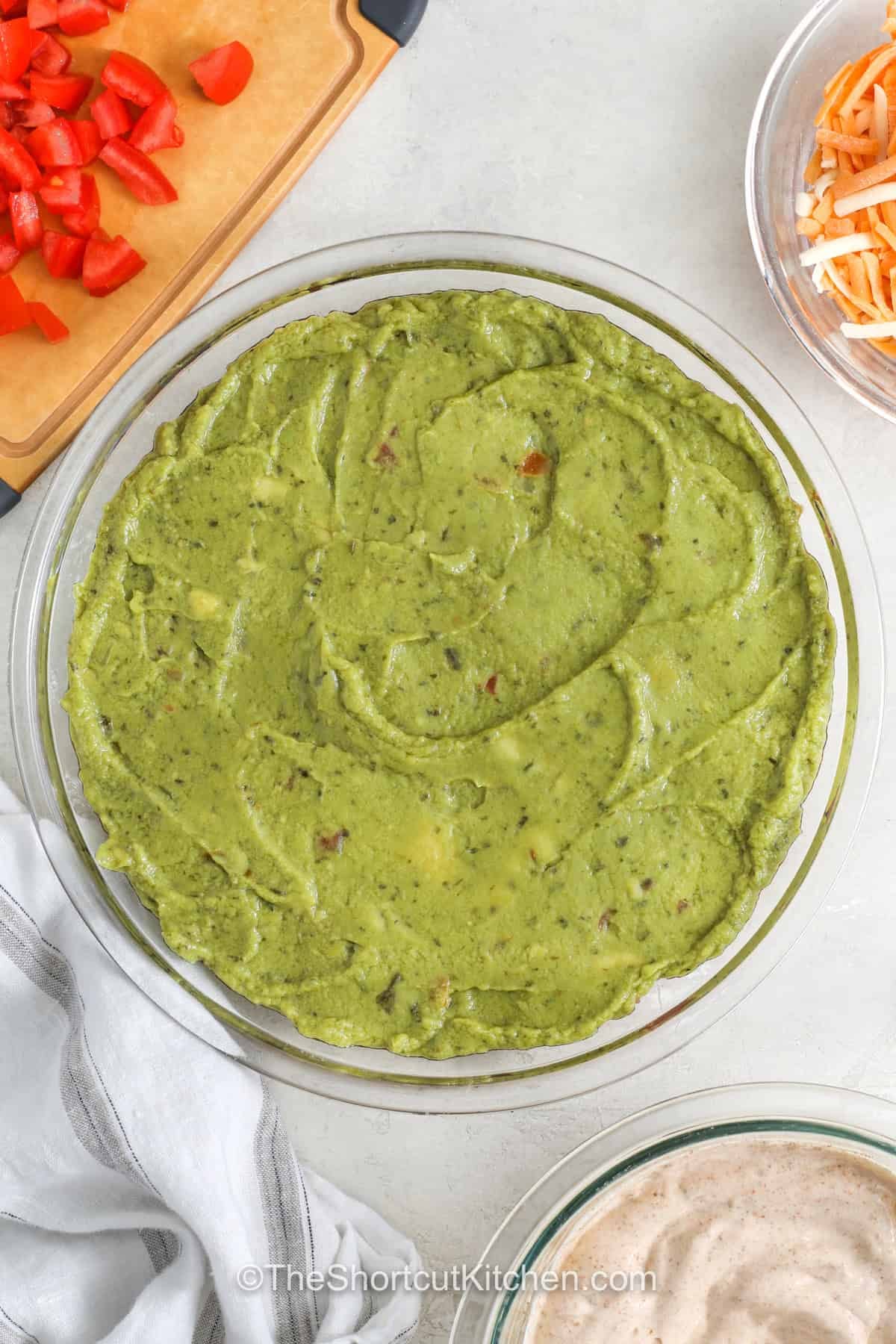 5 layer dip brings together fresh layers of flavor that make every scoop worth reaching for. This easy Mexican dip combines creamy, cheesy, and zesty ingredients into a party appetizer everyone enjoys. It is a great choice for potlucks, holiday gatherings, game day spreads, or casual family snacks. Give this favorite a spot on your table and enjoy every delicious bite. #theshortcutkitchen adding guacamole layer to dish to make 5 Layer Dip