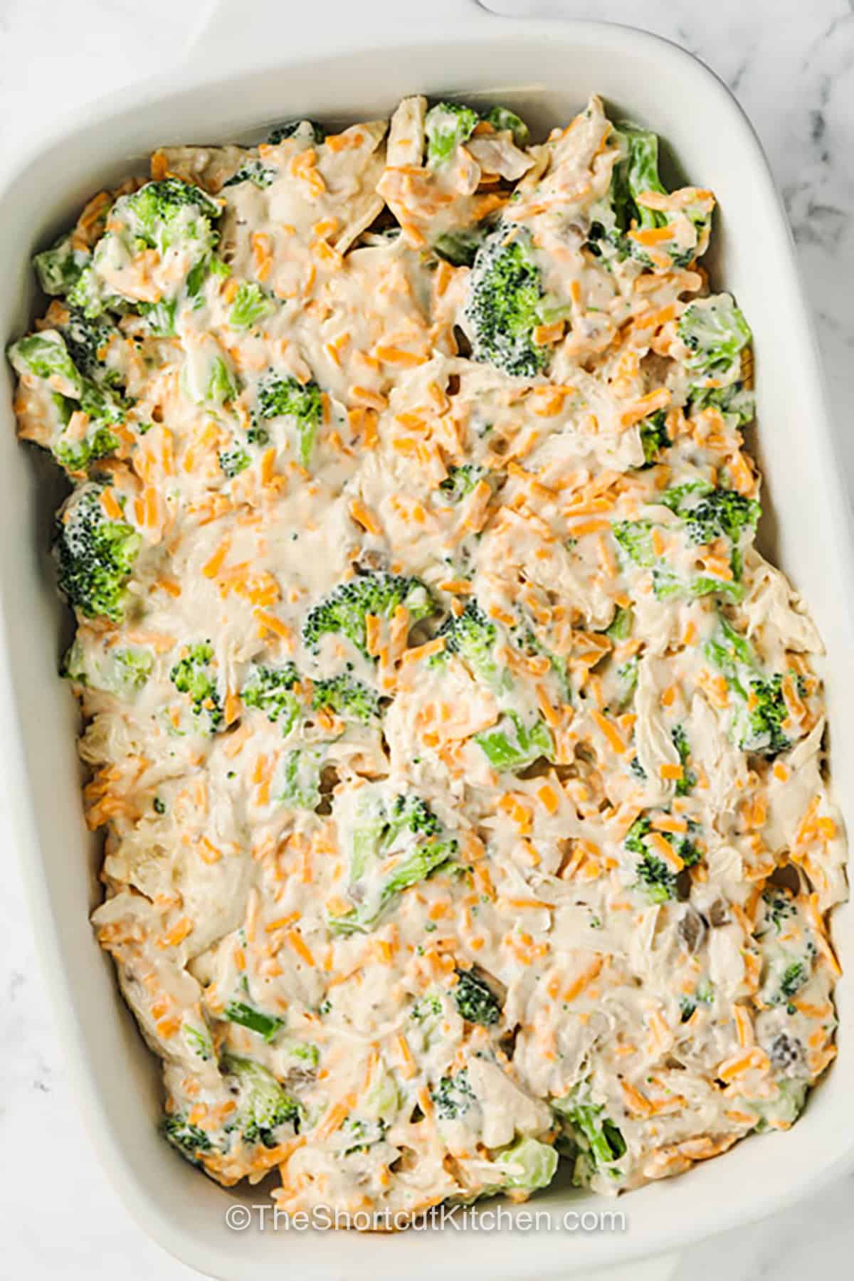 Broccoli chicken casserole is a warm, cheesy dinner made for busy evenings. Frozen broccoli saves chopping, while leftover chicken or chopped rotisserie chicken cuts preparation to about 10 minutes. A creamy mixture of cheddar, mushroom soup, sour cream, mayonnaise, and eggs bakes into a rich filling with a golden cheese topping. This easy chicken casserole also freezes well in portions. Pin it now for a comforting make-ahead meal. #theshortcutkitchen adding Broccoli Chicken Casserole ingredients to casserole dish