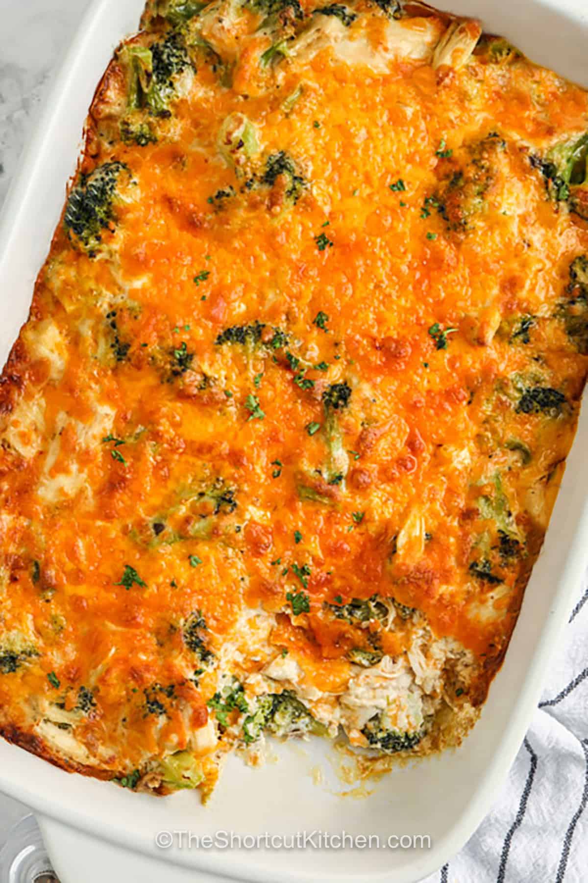 Use cooked chicken and frozen broccoli to make a creamy broccoli chicken casserole without rice or pasta. Sharp cheddar gives the oven-baked casserole bold flavor, while sour cream and mushroom soup create a smooth, savory sauce. It is easy to assemble in one bowl and makes six generous servings. Serve this low carb chicken casserole on its own or add rolls, rice, or salad. Save this cheesy shortcut dinner for later. #theshortcutkitchen cheesy Broccoli Chicken Casserole with a part taken out