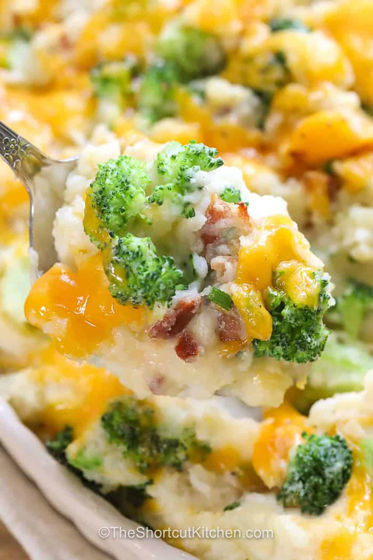 This bacon broccoli potato casserole is creamy, cheesy, and packed with comforting flavor. Mashed russet potatoes make a fluffy base for tender broccoli florets, bacon, cream cheese, sour cream, sharp cheddar, and Parmesan. Bake everything together until piping hot and melted on top. Save this easy casserole recipe when a hearty potato side dish is needed for dinner or entertaining. #theshortcutkitchen taking a spoonful of Broccoli Potato Casserole