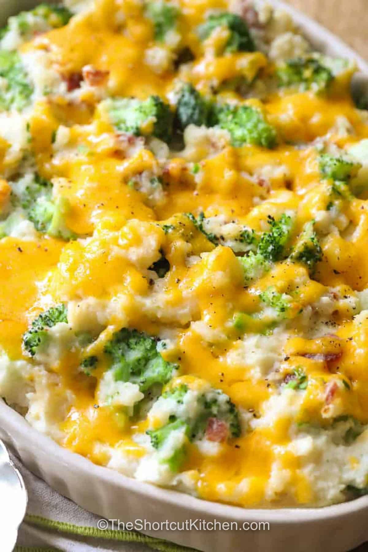 Broccoli potato casserole is a warm and cheesy recipe made with fluffy mashed potatoes, tender-crisp broccoli, bacon, sour cream, and two flavorful cheeses. This simple oven-baked casserole comes together without canned soup or a separate cheese sauce. It is an easy choice for Sunday dinner, a potluck, or a cozy weeknight meal. Save this mashed potato broccoli casserole for later. #theshortcutkitchen caserole dish of Broccoli Potato Casserole