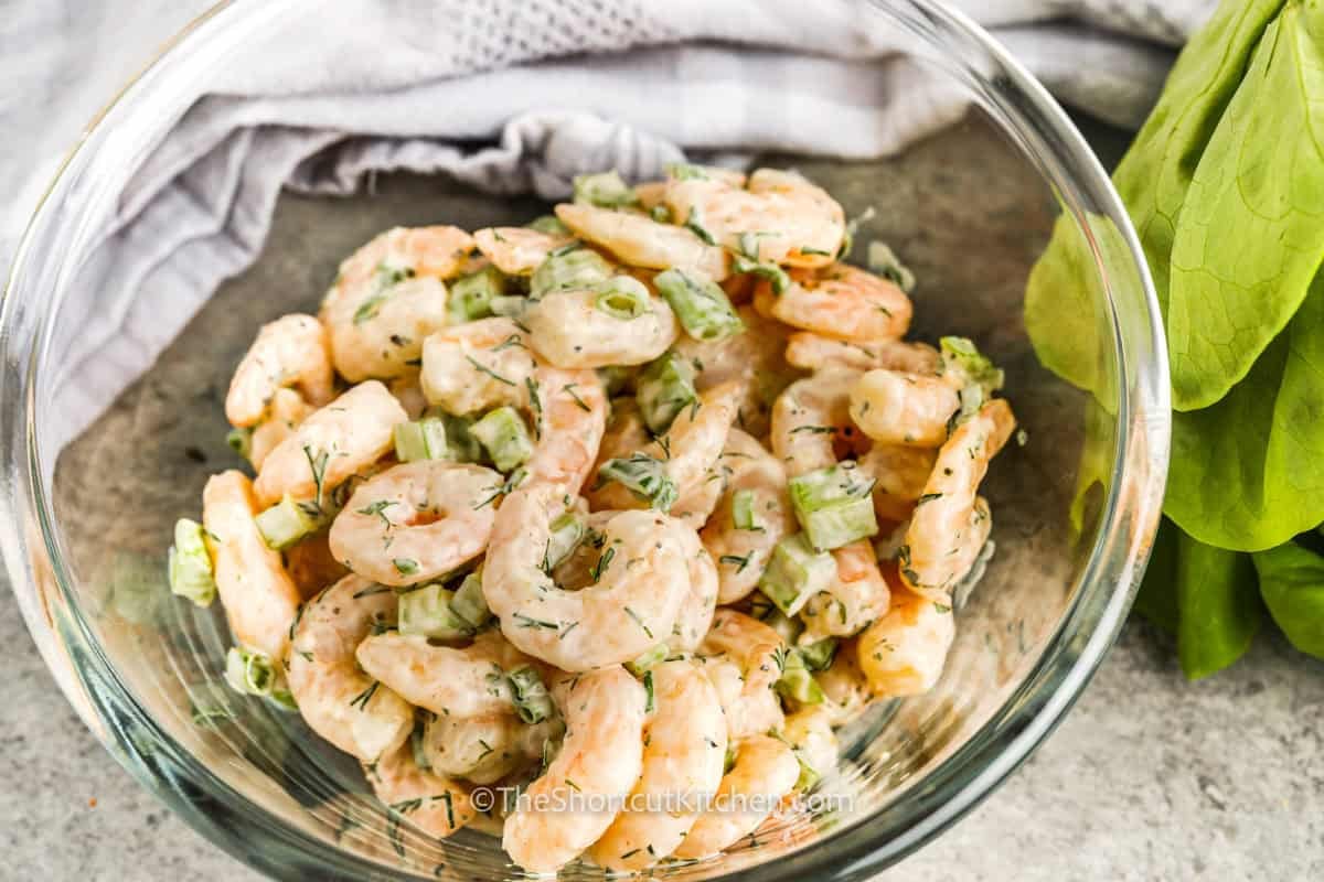 This creamy shrimp salad recipe is a simple way to turn cooked shrimp into a fresh lunch or appetizer. Celery adds crunch, dill adds bright herb flavor, and Old Bay gives the lemon mayo dressing a classic seafood taste. This easy shrimp salad is delicious served cold over lettuce, in lettuce cups, on croissants, or with crackers for a quick make-ahead option. Save this chilled salad idea today. #theshortcutkitchen shrimp salad ingredients with dressing tossed in a bowl