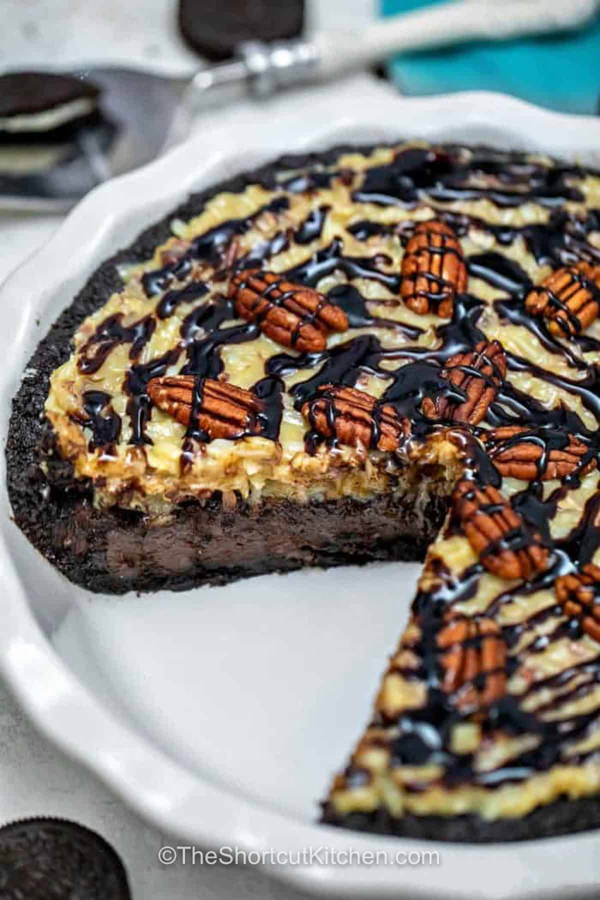This no bake German chocolate pie inspired dessert starts with a no-bake Oreo crust and finishes with rich chocolate filling and classic coconut pecan topping. German sweet chocolate, cocoa powder, heavy cream, pecans, and coconut make every slice creamy, chewy, crunchy, and full of chocolate flavor. Save this pie for a chocolate lover. #theshortcutkitchen German Chocolate Pie with a slice taken out
