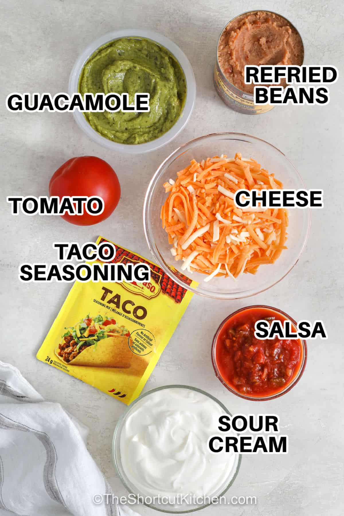 Try this tasty 5 layer dip made with simple ingredients. It comes together in 10 minutes for an appetizer that is delicious served with crunchy tortilla chips or raw veggies. Make it for your next party or potluck and watch it disappear. #theshortcutkitchen refried beans , guacamole , tomato , cheese ,taco seasoning , salsa , sour cream with labels to make 5 Layer Dip