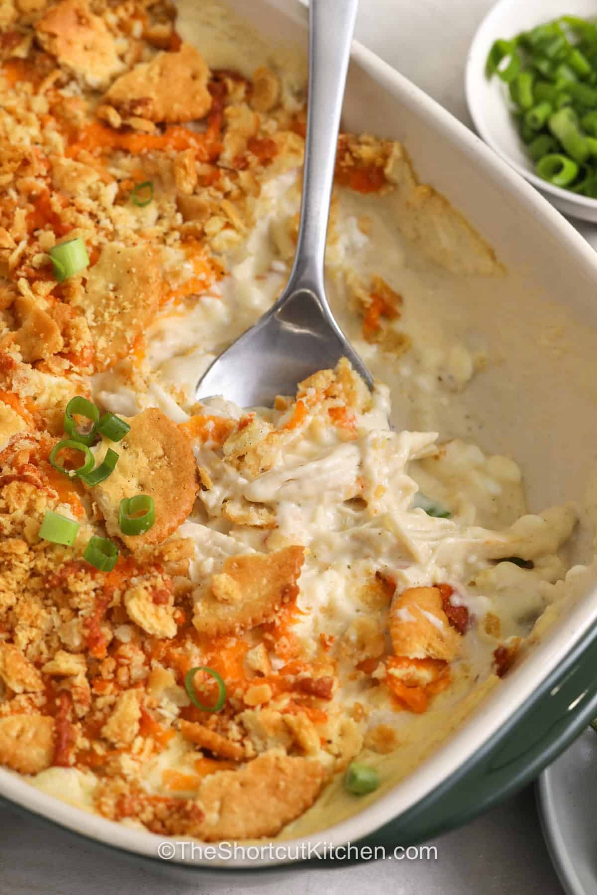 Million dollar chicken casserole is the cheesy chicken recipe your dinner rotation needs. Every spoonful is filled with creamy goodness, savory chicken, and a buttery cracker topping that brings everything together. This comforting casserole is easy to customize and makes great use of cooked chicken. Add this recipe to your favorites and make a delicious dinner your family will ask for again. #theshortcutkitchen close up of creamy Million Dollar Chicken Casserole in the casserole dish