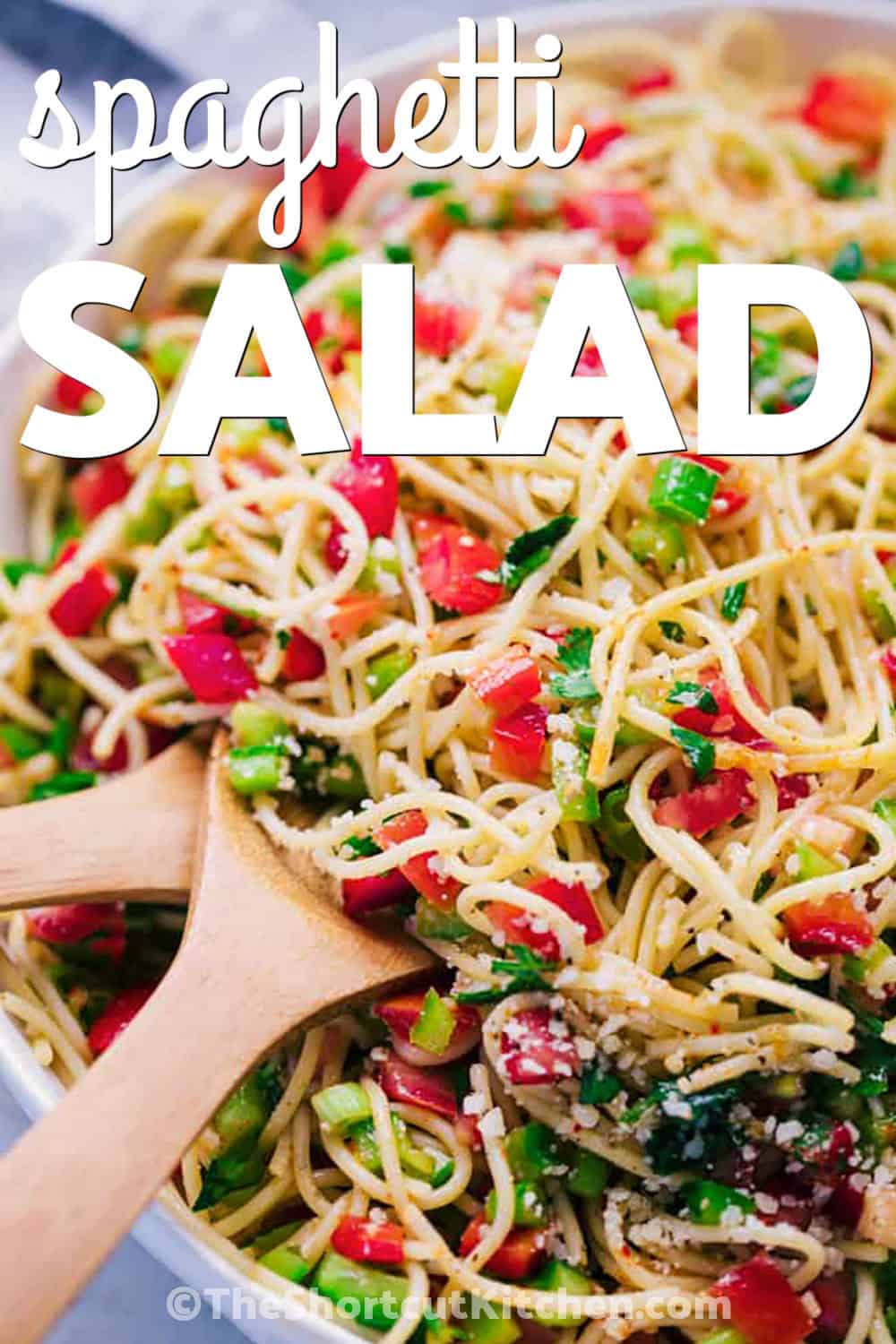 Potluck spaghetti salad is a simple cold pasta salad with spaghetti noodles, crisp peppers, fresh tomatoes, green onions, cilantro, parmesan cheese, and a tangy red wine vinegar dressing. It is budget-friendly, easy to transport, and a great make-ahead side for sharing. Pin it for your next gathering. #theshortcutkitchen close up of Spaghetti Salad in a bowl with wooden spoons and a title