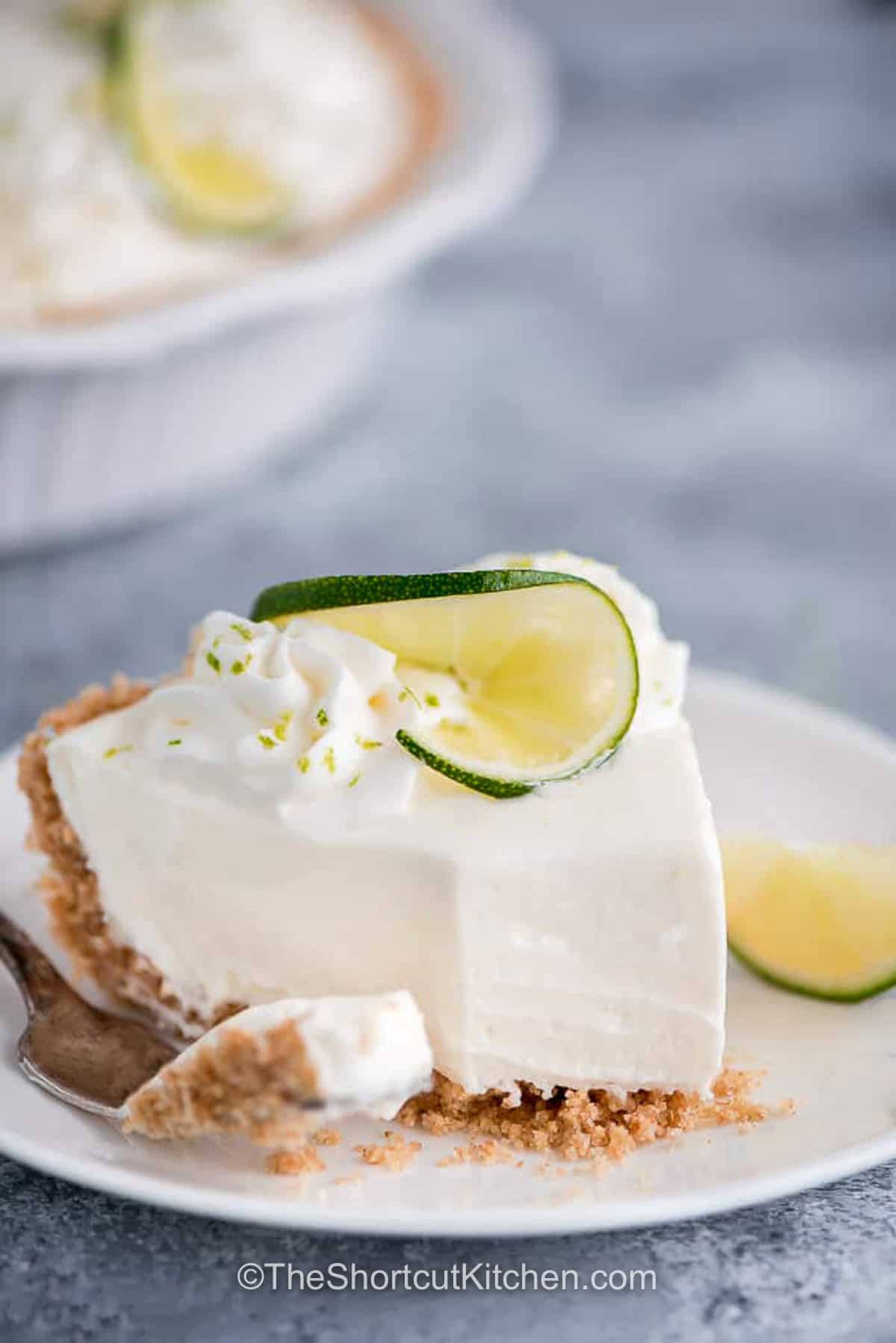 Make this creamy no bake key lime pie with simple ingredients and almost no effort. Fresh lime juice, whipped cream, and cream cheese create a fluffy refrigerator dessert everyone loves. It's the perfect make-ahead treat for cookouts, holidays, and family gatherings. Save this refreshing pie recipe today. #theshortcutkitchen slice of No Bake Key Lime Pie with a bite taken out