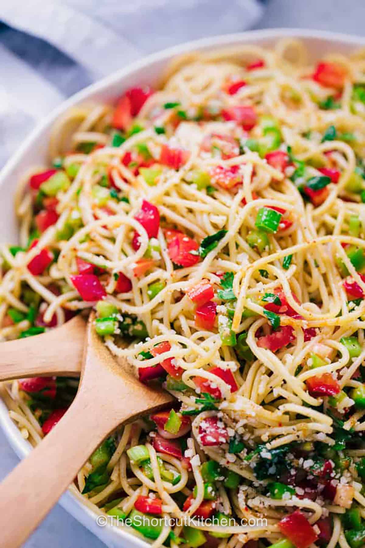 This cold spaghetti salad is loaded with fresh vegetables, parmesan cheese, and a tangy vinaigrette made with oil, red wine vinegar, and seasoning. Spaghetti noodles make it hearty and budget-friendly, while peppers, tomatoes, and cilantro keep every bite fresh, crisp, and flavorful. Save it for potluck season. #theshortcutkitchen Spaghetti Salad in a bowl with wooden spoons