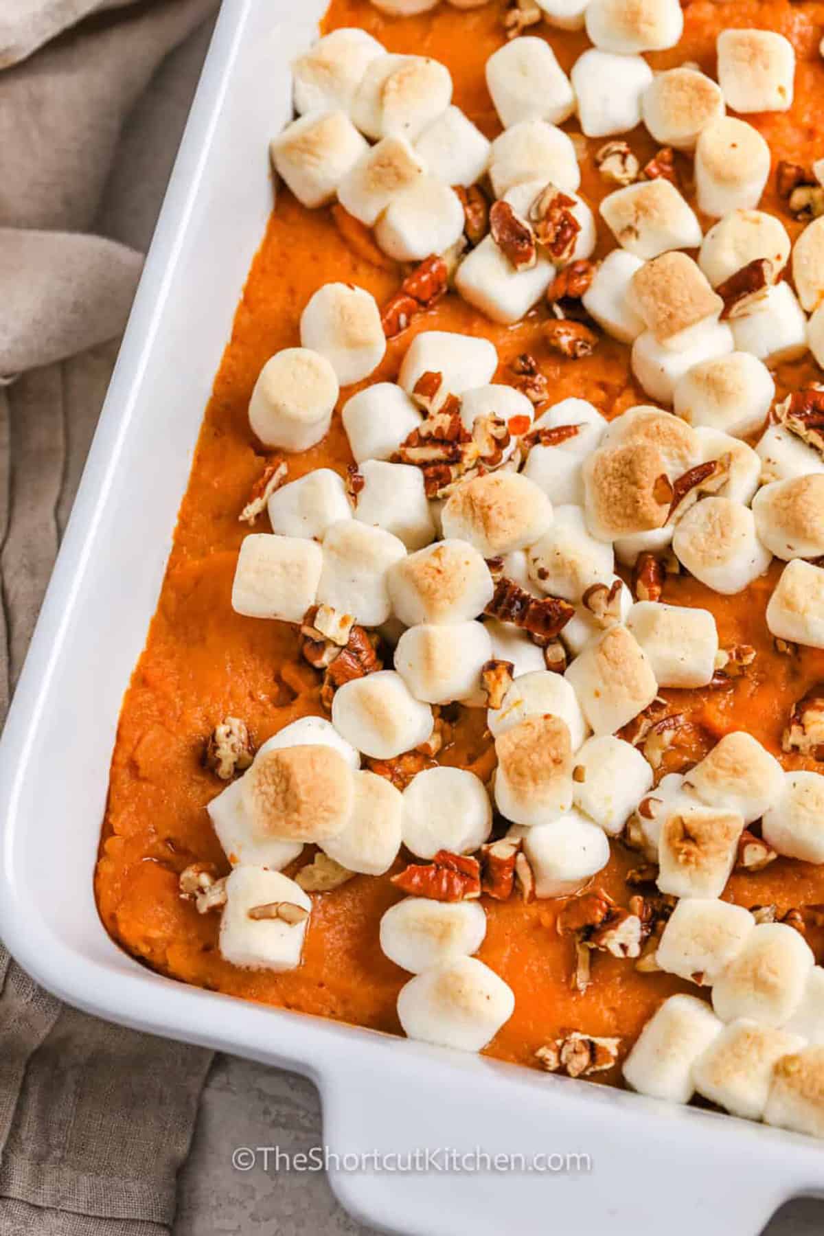 Skip peeling and boiling fresh potatoes with this easy canned sweet potato casserole. Canned yams make the creamy base fast, while heavy cream, brown sugar, cinnamon, and butter give it rich holiday flavor. Mini marshmallows and chopped pecans toast on top as the casserole bakes, giving every serving creamy, gooey, and crunchy textures. Add this sweet potato casserole with marshmallows to your holiday recipe board. #theshortcutkitchen close up of Canned Sweet Potato Casserole.