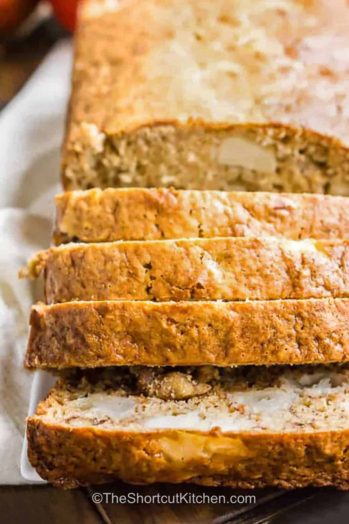 This easy apple banana bread adds juicy chopped apple and crunchy walnuts to a classic banana quick bread. Ripe bananas provide sweetness and moisture, while Greek yogurt helps create a tender crumb and brown sugar adds deeper flavor. Mix the simple batter, pour it into a loaf pan, and bake until golden and tender. It is perfect for using fruit before it goes to waste. Save this moist banana bread with apples recipe today. #theshortcutkitchen loaf of Apple Banana Bread sliced