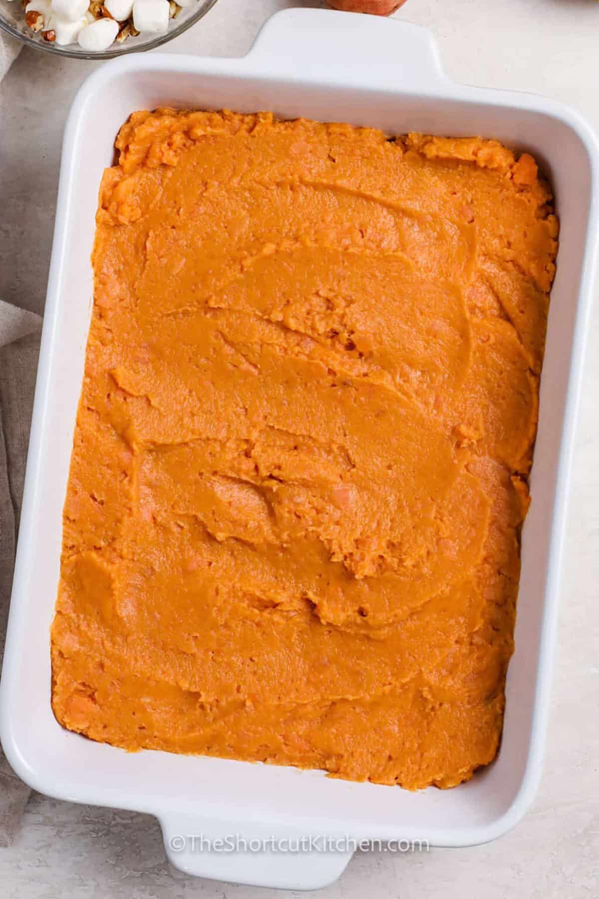 Creamy, buttery, and warmly spiced, canned sweet potato casserole is an easy shortcut for a busy holiday meal. Using canned yams means there are no fresh sweet potatoes to peel or boil. Brown sugar and cinnamon flavor the smooth filling, while mini marshmallows and pecans add a gooey, crunchy oven-baked topping. Make it ahead for Thanksgiving or Christmas. Pin this easy sweet potato casserole for later. #theshortcutkitchen adding sweet potato mixture to dish to make Canned Sweet Potato Casserole.