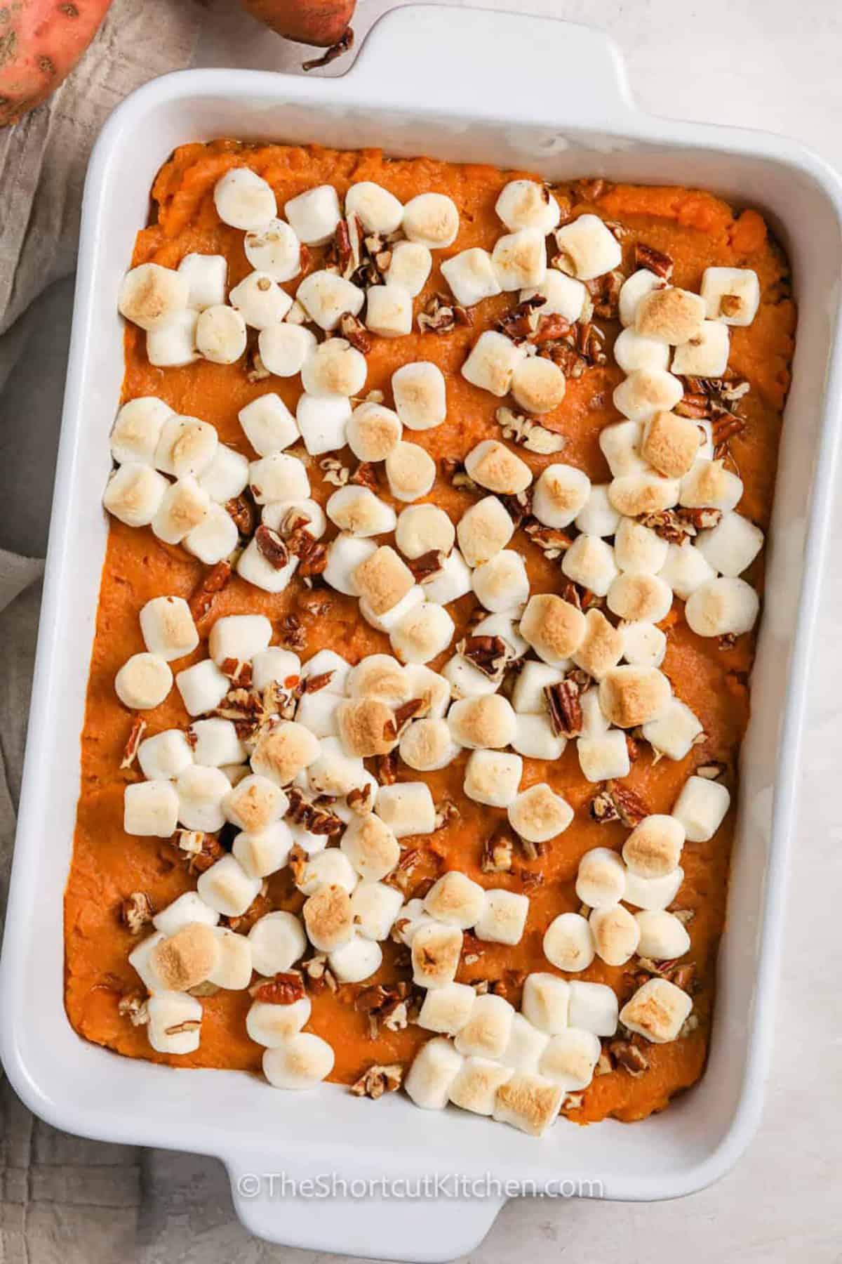 This canned sweet potato casserole has everything to love about the traditional holiday side with much less prep. Canned sweet potatoes are mashed with cream, butter, brown sugar, egg, and cinnamon, then oven baked beneath gooey mini marshmallows and buttery pecans. The easy sweet potato casserole takes about 35 minutes from start to finish and serves eight. Save this recipe for Thanksgiving or Christmas dinner. #theshortcutkitchen baked Canned Sweet Potato Casserole in the dish.