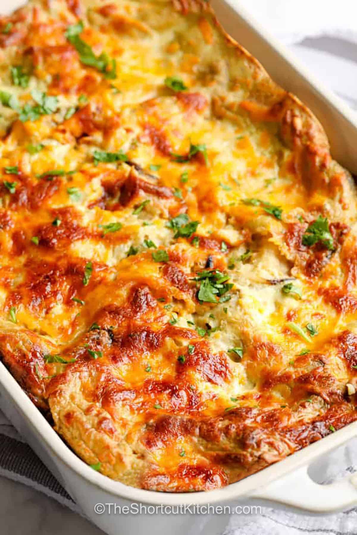 Rotisserie chicken makes this chicken enchilada casserole even faster to prepare. Layers of tortillas, creamy green enchilada sauce, seasoned chicken, and melted cheese bake into a comforting dinner that's ideal for busy families. Save this easy casserole recipe. #theshortcutkitchen casserole dish of Chicken Enchilada Casserole