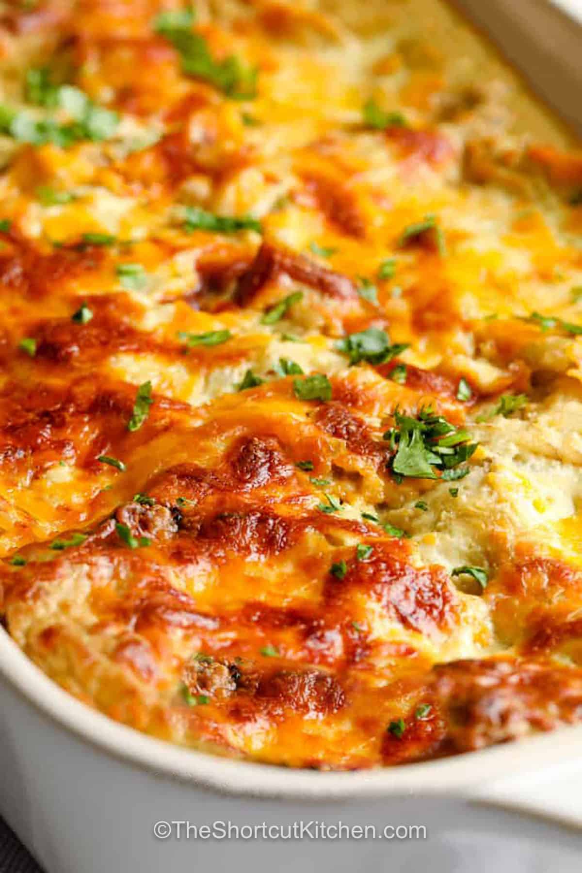 This easy chicken enchilada casserole combines shredded chicken, green enchilada sauce, corn tortillas, Monterey Jack cheese, and a creamy sauce for an easy baked dinner. Skip rolling enchiladas and enjoy all the same flavors in one comforting casserole. Perfect for busy weeknights, meal prep, and freezer meals. Save this recipe for your next family dinner. #theshortcutkitchen close up of Chicken Enchilada Casserole.