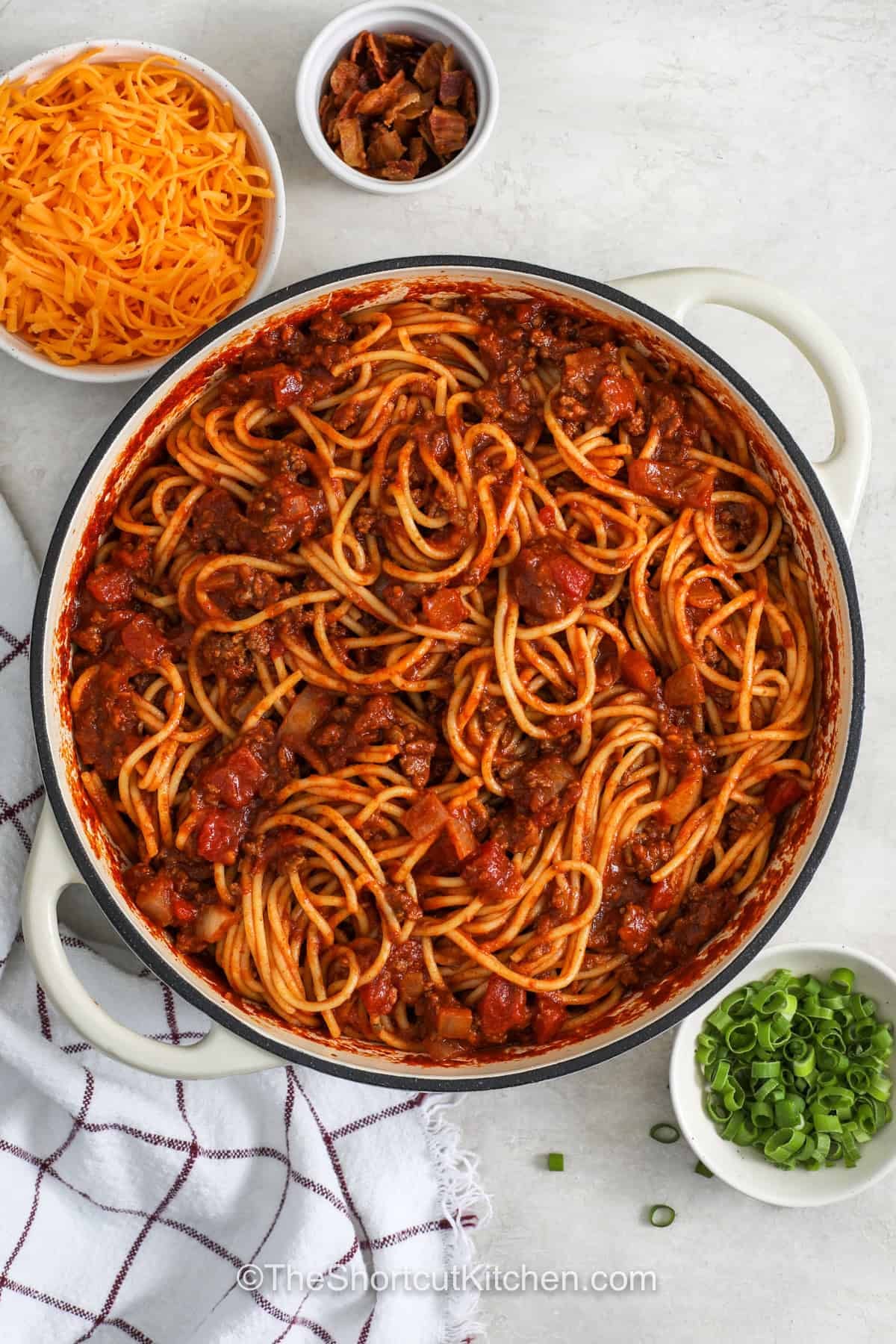 Cowboy spaghetti is a hearty pasta dinner loaded with ground beef, tomato sauce, and chili-seasoned flavor. Tender spaghetti is tossed with a rich beef sauce and diced tomatoes with chilies for a family-friendly meal. Top each serving with cheddar, bacon bits, and green onions for extra flavor. Make this easy comfort food tonight. #theshortcutkitchen top view of Cowboy Spaghetti