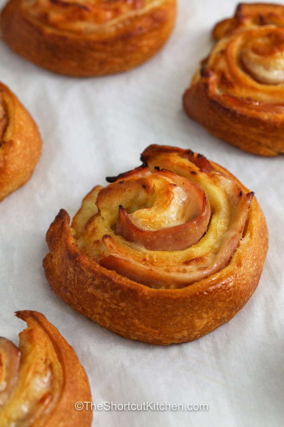 Ham and cheese pinwheels are packed with savory flavor and make an easy appetizer for any occasion. Honey mustard adds a tangy layer beneath the ham and Swiss cheese, while crescent dough gives each pinwheel a golden baked finish. A little garlic butter makes these tasty bites even more delicious. Serve them warm for parties, family gatherings, lunch, or game day. Roll up a batch and enjoy them today. #theshortcutkitchen close up of Ham and Cheese Pinwheels