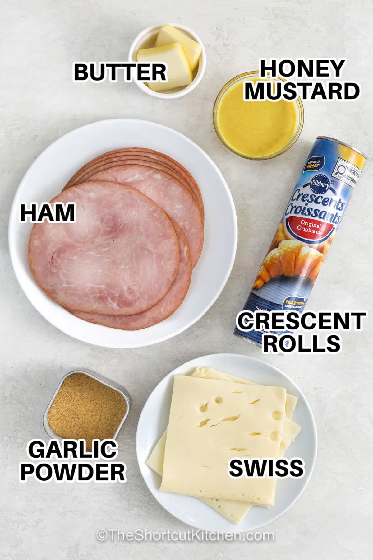 Ham and cheese pinwheels make a tasty snack with just a handful of everyday ingredients. Flaky crescent dough wraps around sliced ham, Swiss cheese, and flavorful honey mustard for a simple appetizer that is hard to resist. The pinwheels bake until golden, and the cheese is warm and melty. They are perfect for parties, holiday trays, lunch boxes, or casual snacking. Bake these delicious pinwheels for your next gathering. #theshortcutkitchen Swiss cheese ,garlic powder , crescent rolls , ham , honey mustard , butter with labels to make Ham and Cheese Pinwheels
