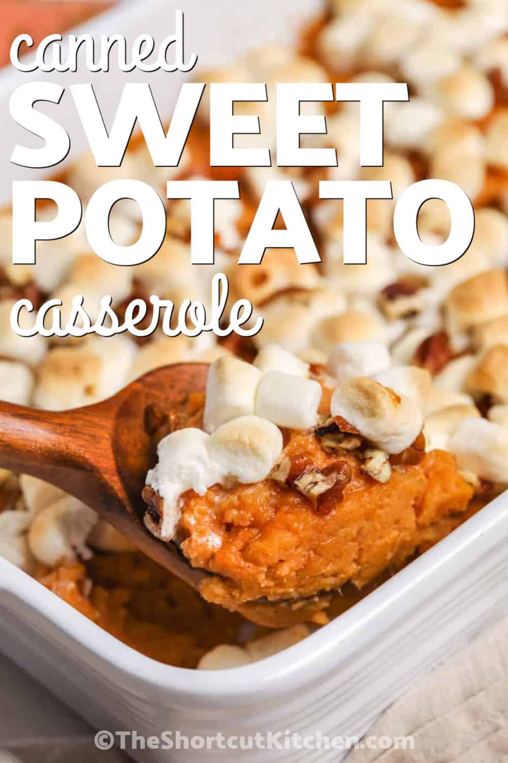 Skip peeling and boiling fresh potatoes with this easy canned sweet potato casserole. Canned yams make the creamy base fast, while heavy cream, brown sugar, cinnamon, and butter give it rich holiday flavor. Mini marshmallows and chopped pecans toast on top as the casserole bakes, giving every serving creamy, gooey, and crunchy textures. Add this sweet potato casserole with marshmallows to your holiday recipe board. #theshortcutkitchen Canned Sweet Potato Casserole on a wooden spoon with casserole dish full and a title.