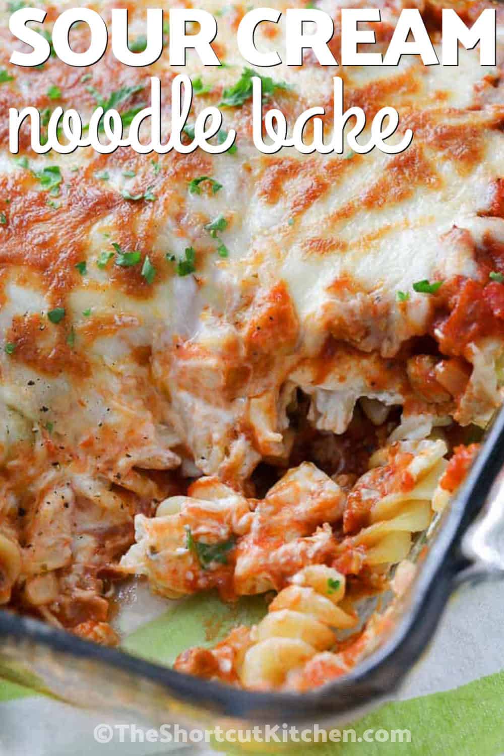 Sour cream noodle bake is an easy oven-baked casserole made with seasoned ground beef, rotini, pasta sauce, sour cream, cream cheese, Parmesan, and plenty of melted mozzarella. The layers bake together into a creamy, saucy comfort-food dinner with just 15 minutes of prep. Save this easy casserole for busy weeknights, family dinners, or meal prep. Pin the recipe and make it tonight. #theshortcutkitchen Sour Cream Noodle Bake with a title