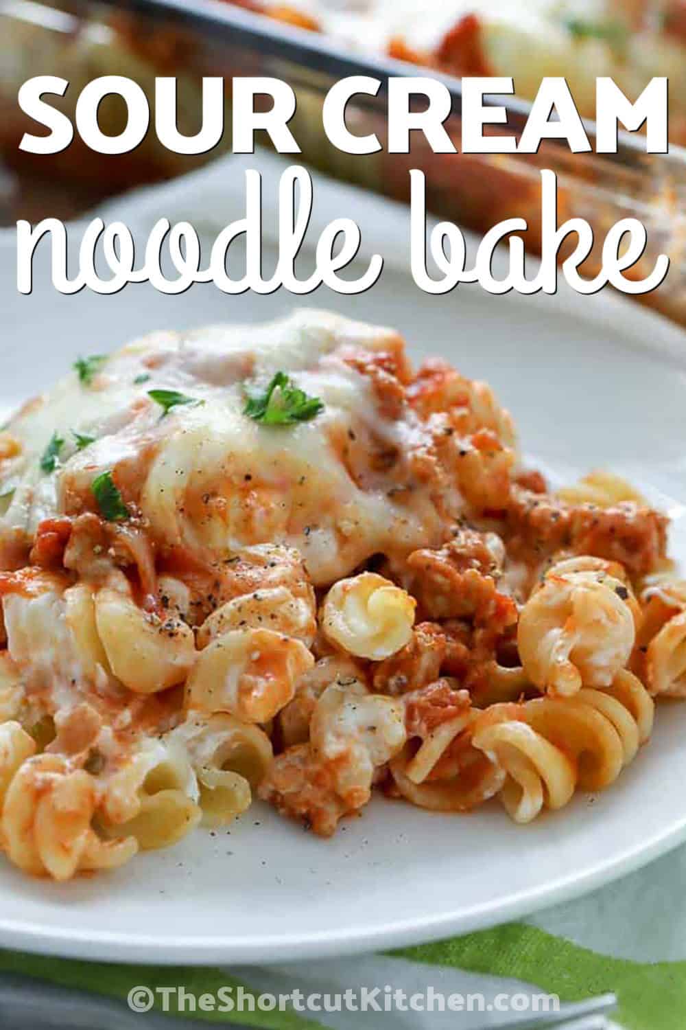 Sour cream noodle bake is loaded with everything a comforting pasta dinner needs. Savory ground beef and pasta sauce surround tender rotini and a creamy sour cream, cream cheese, and Parmesan layer, while mozzarella melts over the top. This oven-baked casserole is easy to assemble and ready in just 35 minutes. Pin this easy cheesy casserole for your next weeknight dinner. #theshortcutkitchen plated Sour Cream Noodle Bake with writing
