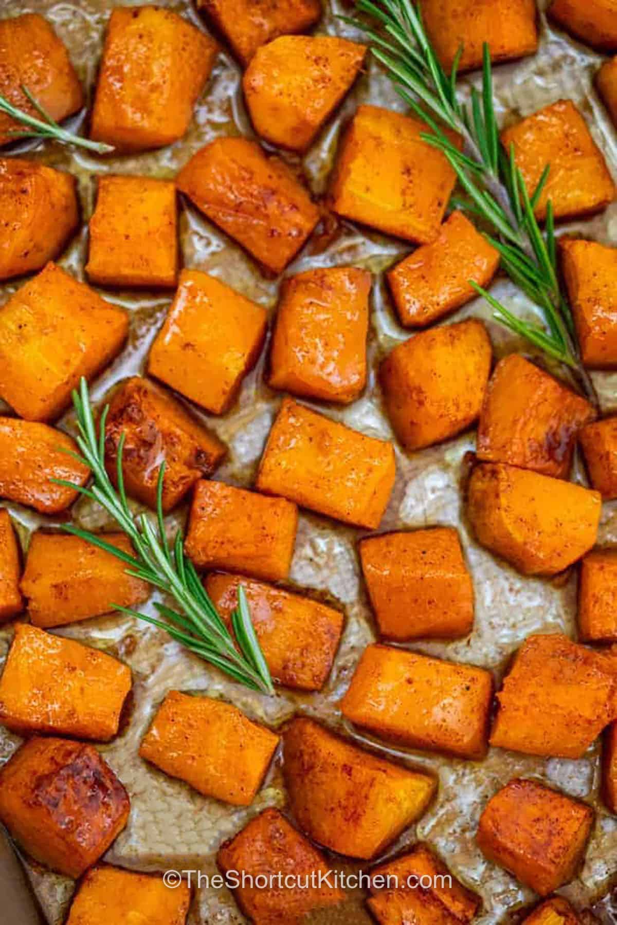 Sweet oven roasted butternut squash is easy to make with a handful of ingredients and one sheet pan. Butternut squash cubes roast with maple syrup, cinnamon, nutmeg, and optional brown sugar until tender and golden, then fresh rosemary adds an earthy finish. It's an easy roasted butternut squash recipe for Thanksgiving, fall dinners, or simple weeknight meals. Pin this recipe for your next cozy dinner. #theshortcutkitchen Oven Roasted Butternut Squash on a sheet pan