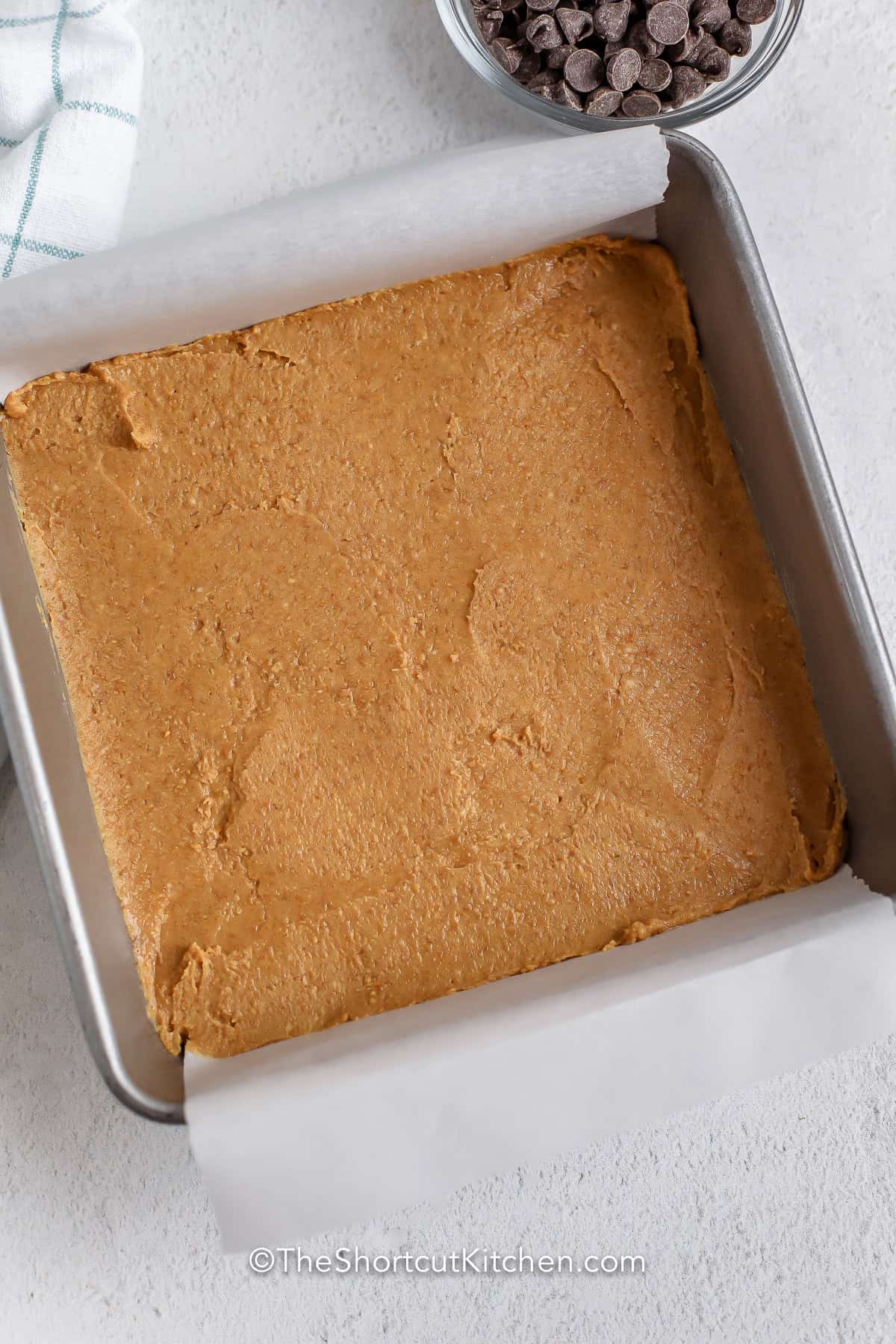 Looking for the best peanut butter bars recipe? These easy no-bake bars are made with pantry staples and topped with rich chocolate for a dessert everyone loves. Sometimes called a Gold Bars Recipe, they're quick to prepare, easy to freeze, and ideal for holiday baking or anytime cravings. Pin this recipe for later. #theshortcutkitchen adding peanut butter mixture to pan to make Peanut Butter Bars
