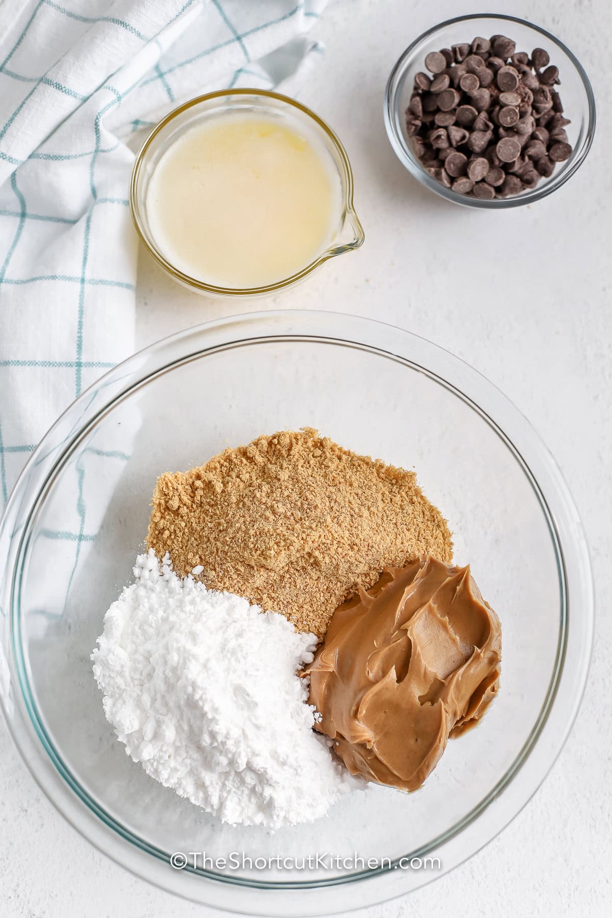 Skip the oven and make these creamy peanut butter bars recipe with graham crackers, peanut butter, butter, and chocolate. This shortcut dessert is simple enough for beginners and always disappears fast at family gatherings. Save this easy no-bake dessert today. #theshortcutkitchen adding ingredients together in bowl to make Peanut Butter Bars