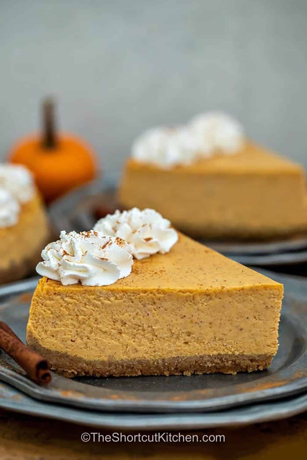 This pumpkin pie cheesecake has everything to love about a cozy fall dessert. A pumpkin spice graham cracker crust holds a rich filling made with cream cheese and pumpkin pie filling, then the cheesecake is gently baked in a water bath. Chill it overnight and decorate with whipped cream, cinnamon, and caramel before serving. Save this easy pumpkin cheesecake for Thanksgiving and fall entertaining. #theshortcutkitchen slice of Pumpkin Pie Cheesecake plated
