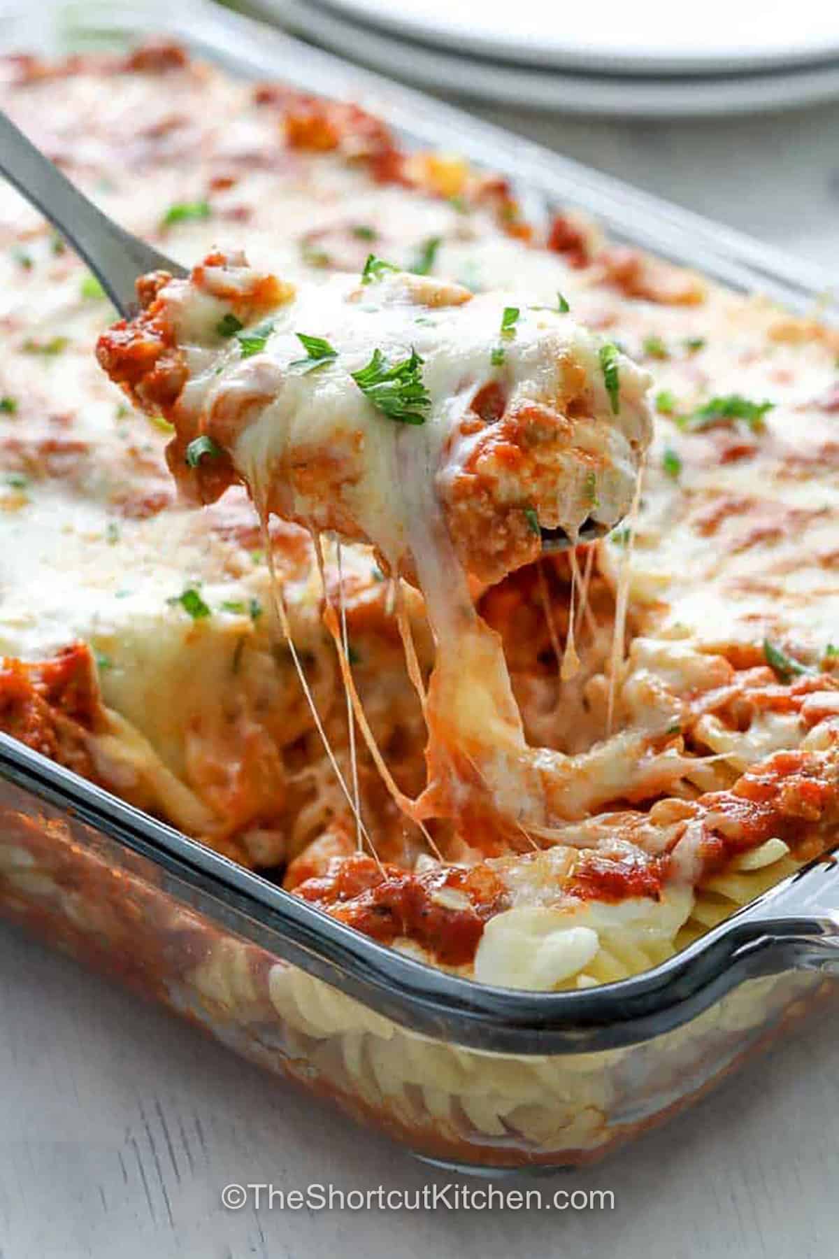 This sour cream noodle bake turns simple ingredients into cozy comfort food. Ground beef, rotini, jarred pasta sauce, sour cream, cream cheese, Parmesan, and mozzarella are layered in a casserole dish and baked until creamy and bubbling. It's an easy ground beef pasta casserole that's filling enough for family dinner and simple enough for busy nights. Save this oven-baked noodle casserole for later. #theshortcutkitchen taking Sour Cream Noodle Bake out of the dish