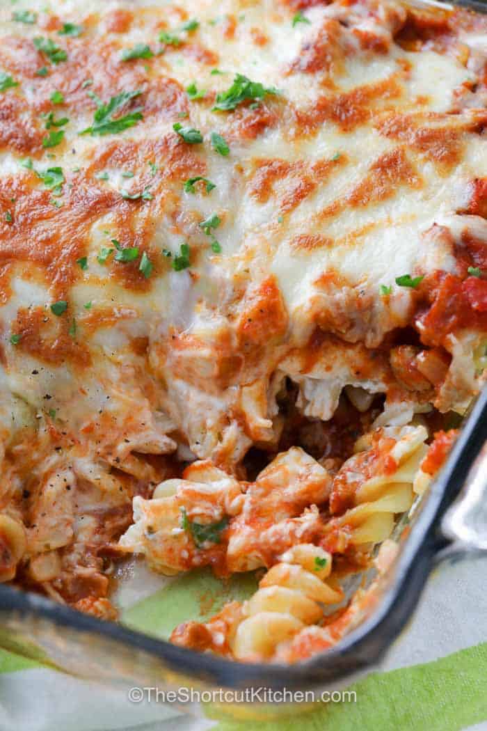 Add sour cream noodle bake to the list of easy casseroles worth keeping on repeat. This oven-baked dinner layers ground beef and tomato sauce with tender rotini, tangy sour cream, rich cream cheese, Parmesan, and lots of mozzarella. It comes together quickly with everyday ingredients and makes a hearty family-sized meal. Save this cheesy ground beef pasta casserole and try it this week. #theshortcutkitchen Sour Cream Noodle Bake in the dish with a portion taken out