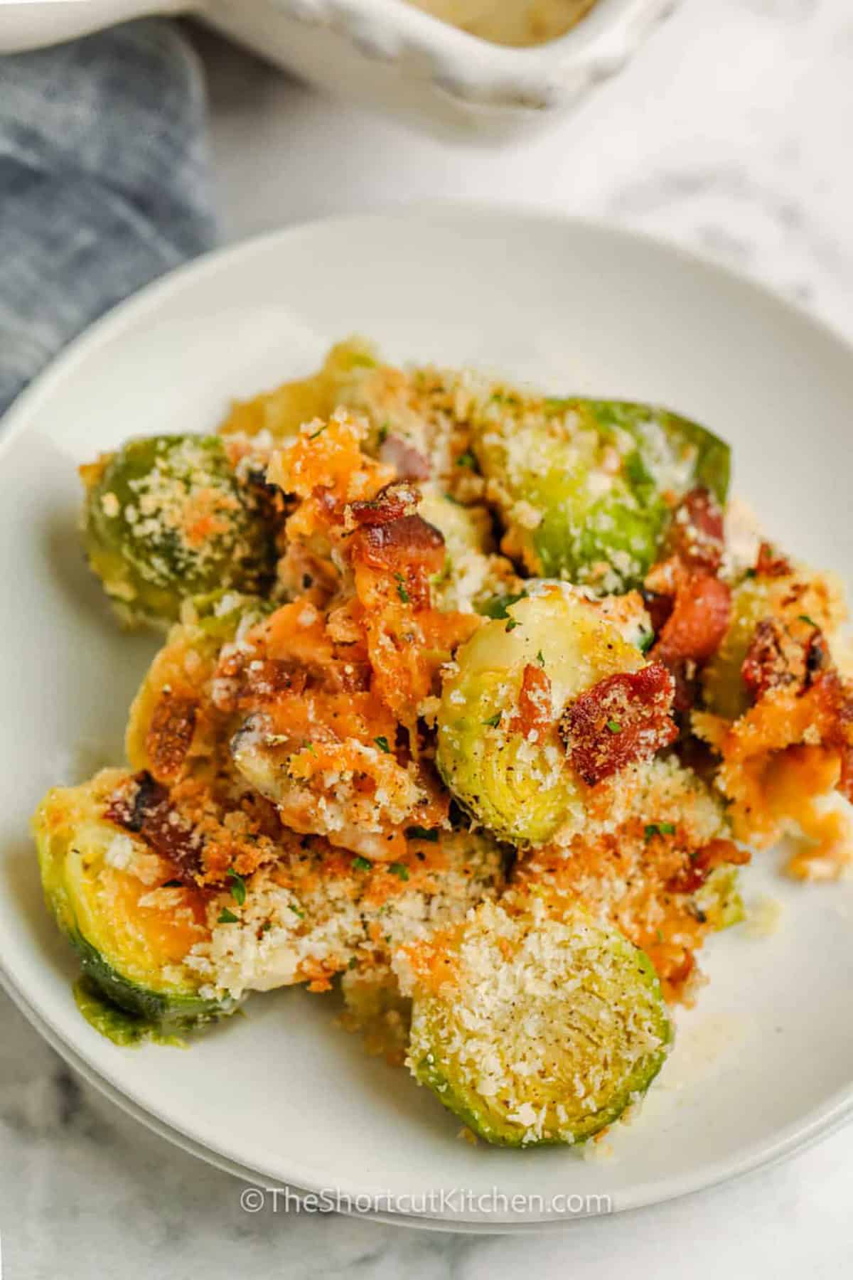 Easy Brussel sprout casserole is a creamy oven-baked side made with fresh Brussels sprouts, crisp bacon, cheddar cheese, heavy cream, and panko breadcrumbs. Every serving has tender sprouts underneath and a crunchy golden topping. Ready in just 30 minutes, this Brussels sprouts casserole with bacon works for busy dinners and holiday entertaining. Save this easy side dish recipe and make it soon. #theshortcutkitchen plated Brussel Sprout Casserole.