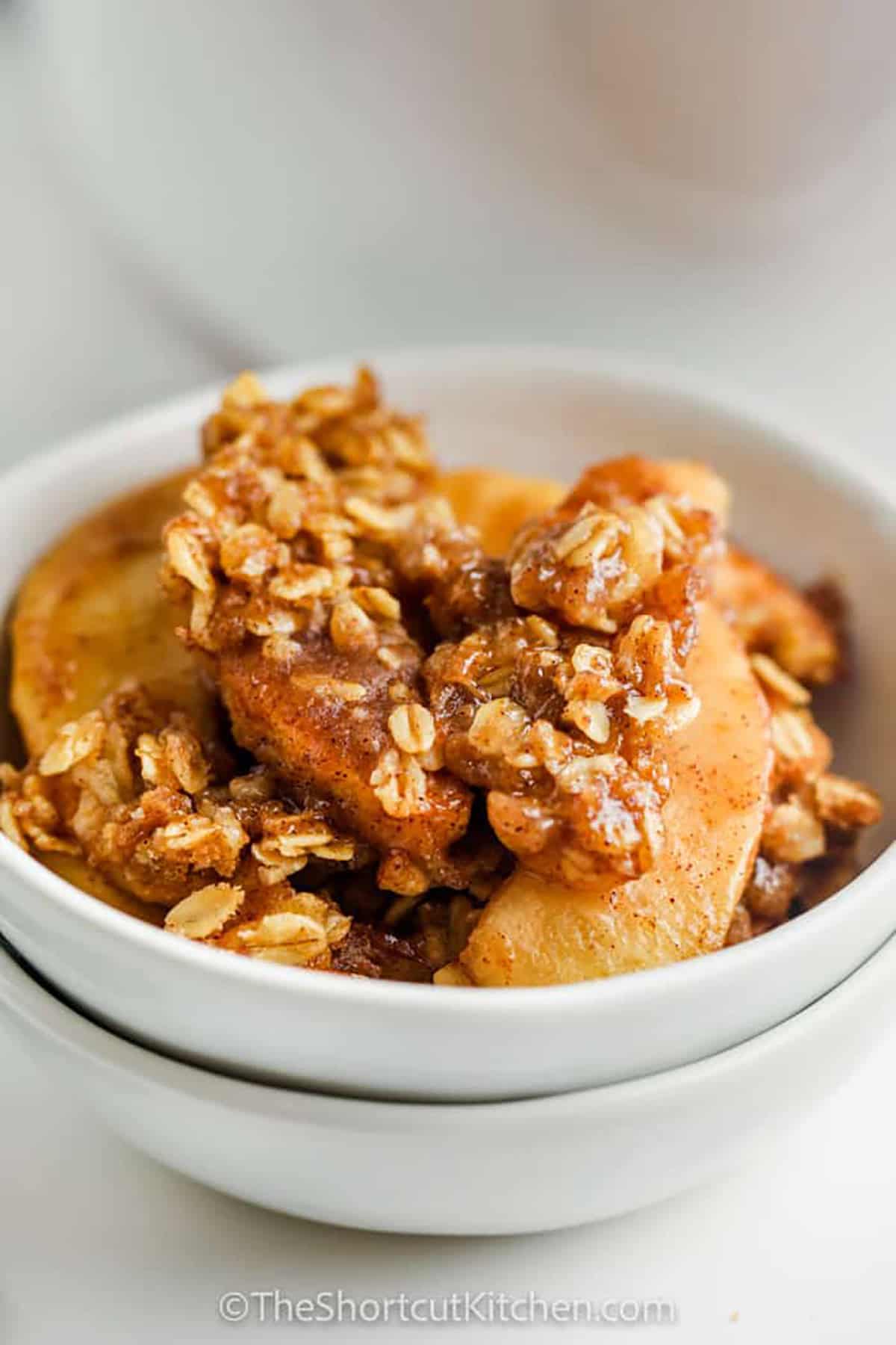 Fresh apples and warm cinnamon make this Slow Cooker apple crisp a cozy dessert for cool-weather dinners. A buttery mixture of brown sugar, flour, and old-fashioned oats forms the crumble topping while the crockpot gently cooks the apples underneath. With just 15 minutes of prep, this easy apple crisp is simple enough for any day of the week. Pin this crockpot apple dessert and make it soon! #theshortcutkitchen bowl of Crock Pot Apple Crisp