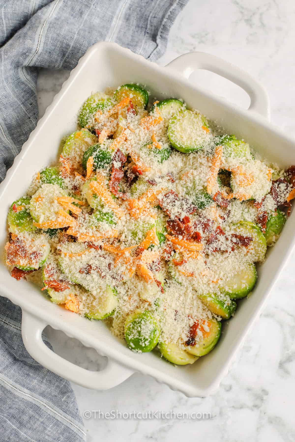 Cheesy Brussel sprout casserole is packed with tender Brussels sprouts, savory bacon, melted cheddar, and a crisp panko topping. A quick boil gives the sprouts a head start before everything is mixed and baked until creamy and bubbly. Serve this easy Brussels sprout casserole alongside roast turkey or ham for Thanksgiving, Christmas, or Sunday dinner. Save this cozy vegetable casserole for the holidays. #theshortcutkitchen Brussel Sprout Casserole in the dish before cooking.