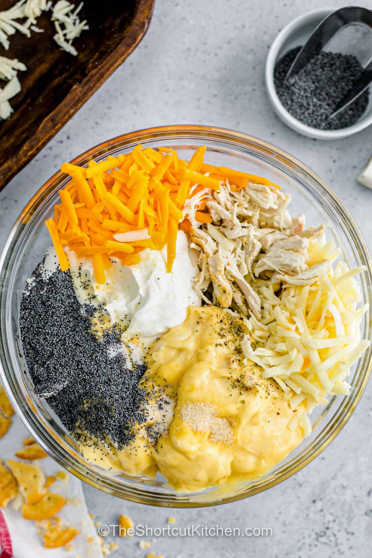Turn leftover chicken into chicken poppyseed casserole with almost no prep. This oven-baked casserole combines shredded chicken, Greek yogurt, cream of chicken soup, two cheeses, lemon, poppy seeds, and simple seasonings under buttery crushed Ritz crackers. The filling stays creamy while the topping turns crisp and golden. Serve this easy chicken casserole with rice or green beans. Add it to your weeknight dinner board. #theshortcutkitchen adding ingredients to bowl to make Chicken Poppyseed Casserole.