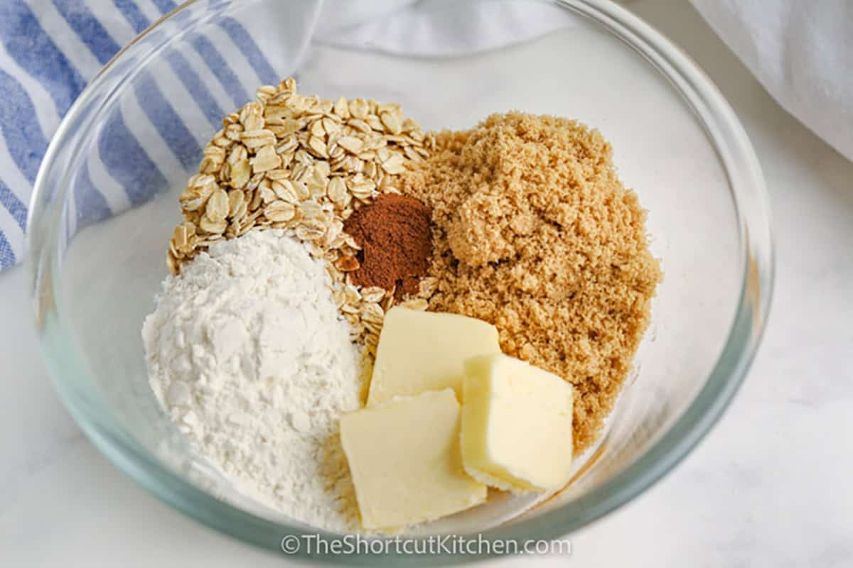 Slow Cooker apple crisp is an easy way to enjoy warm, cinnamon-spiced apples without using the oven. Fresh apples cook beneath a brown sugar, butter, flour, and old-fashioned oat crumble for a comforting dessert with classic fall flavor. Prep takes just 15 minutes, making Slow Cooker crisp perfect for busy days and holiday dinners. Save this simple apple dessert recipe and make it this fall. #theshortcutkitchen adding ingredients together for Crock Pot Apple Crisp