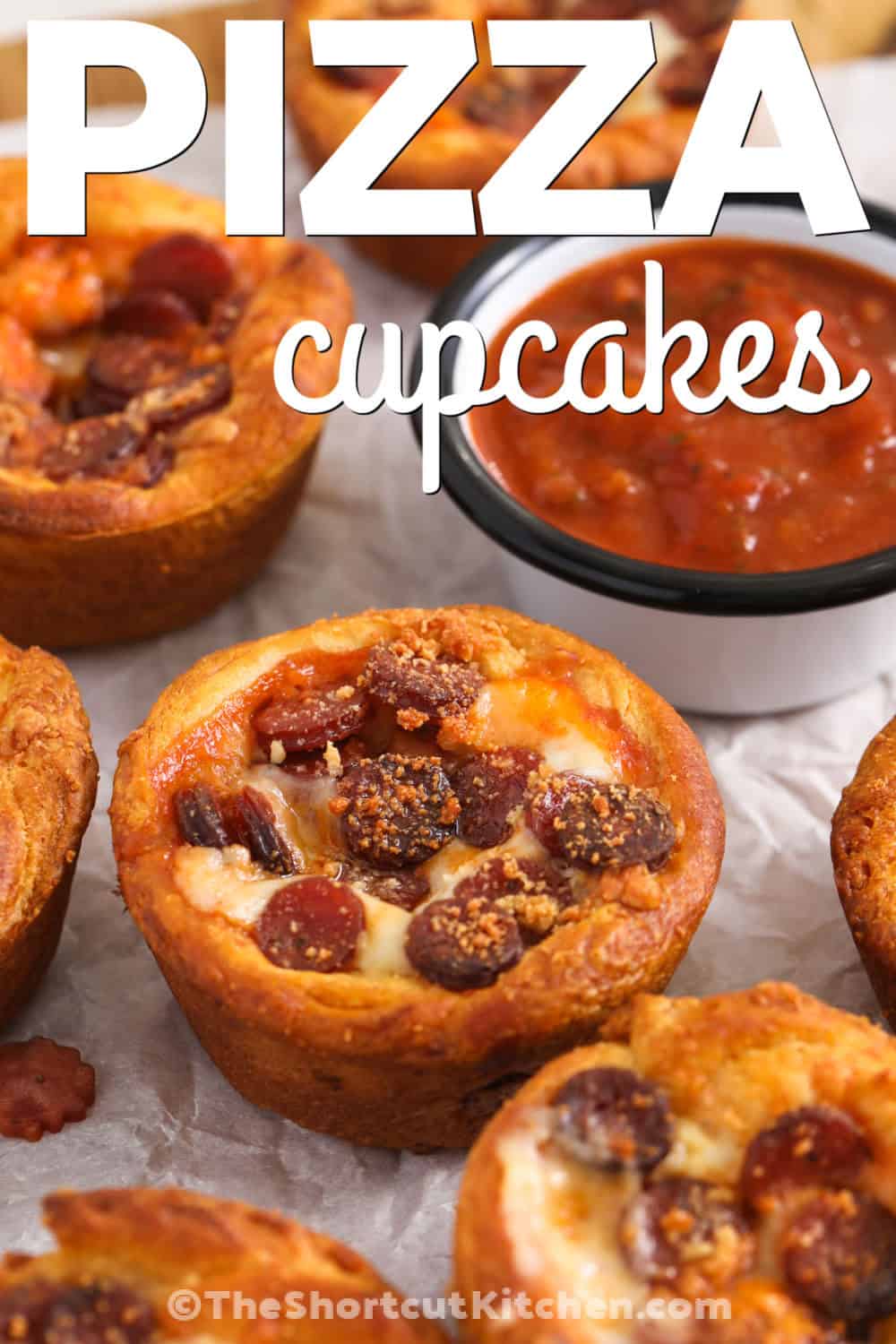 These pizza cupcakes turn simple crescent roll dough into a fun handheld pizza snack. Pizza sauce, mozzarella, pepperoni, and Parmesan come together in each golden cup for plenty of classic flavor. They are easy to customize with your favorite toppings and make a tasty appetizer, lunch, or after-school snack. Keep this easy muffin tin recipe handy for busy days. Give these pizza cupcakes a try today. #theshortcutkitchen Pizza Cupcakes with marinara and a title.