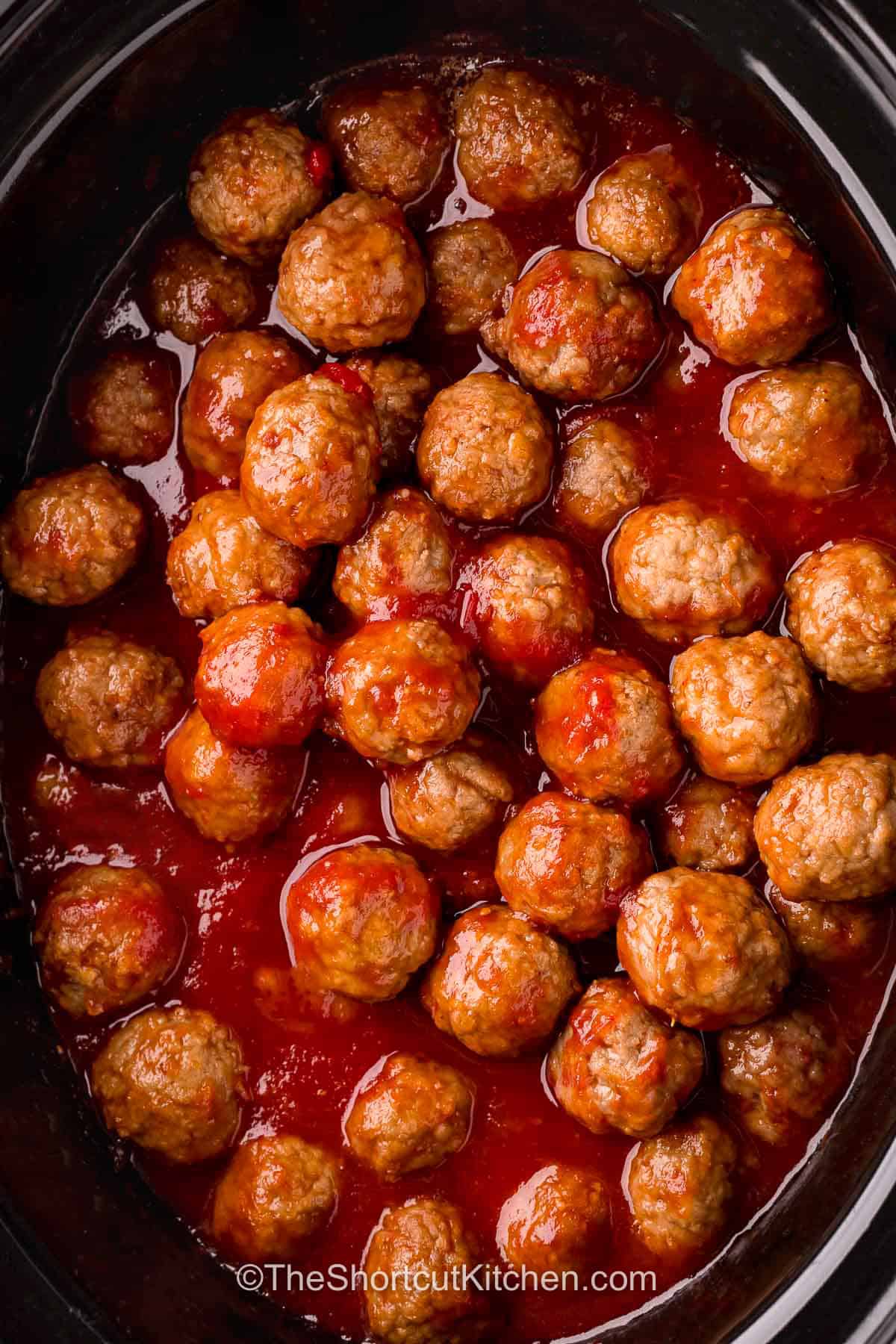 Pepper jelly meatballs are a delicious way to make your appetizer spread more exciting. Juicy meatballs are coated in a sweet, tangy, and spicy sauce made with raspberry jam, chili sauce, and red pepper jelly. This easy slow cooker appetizer is perfect for serving at parties because it stays warm and ready for guests. Pair them with toothpicks for simple, mess-free serving. Add these flavorful meatballs to your next gathering and make entertaining easier. #theshortcutkitchen Pepper Jelly Meatballs in the slow cooker.