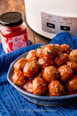 plate of Pepper Jelly Meatballs with slow cooker in the background.