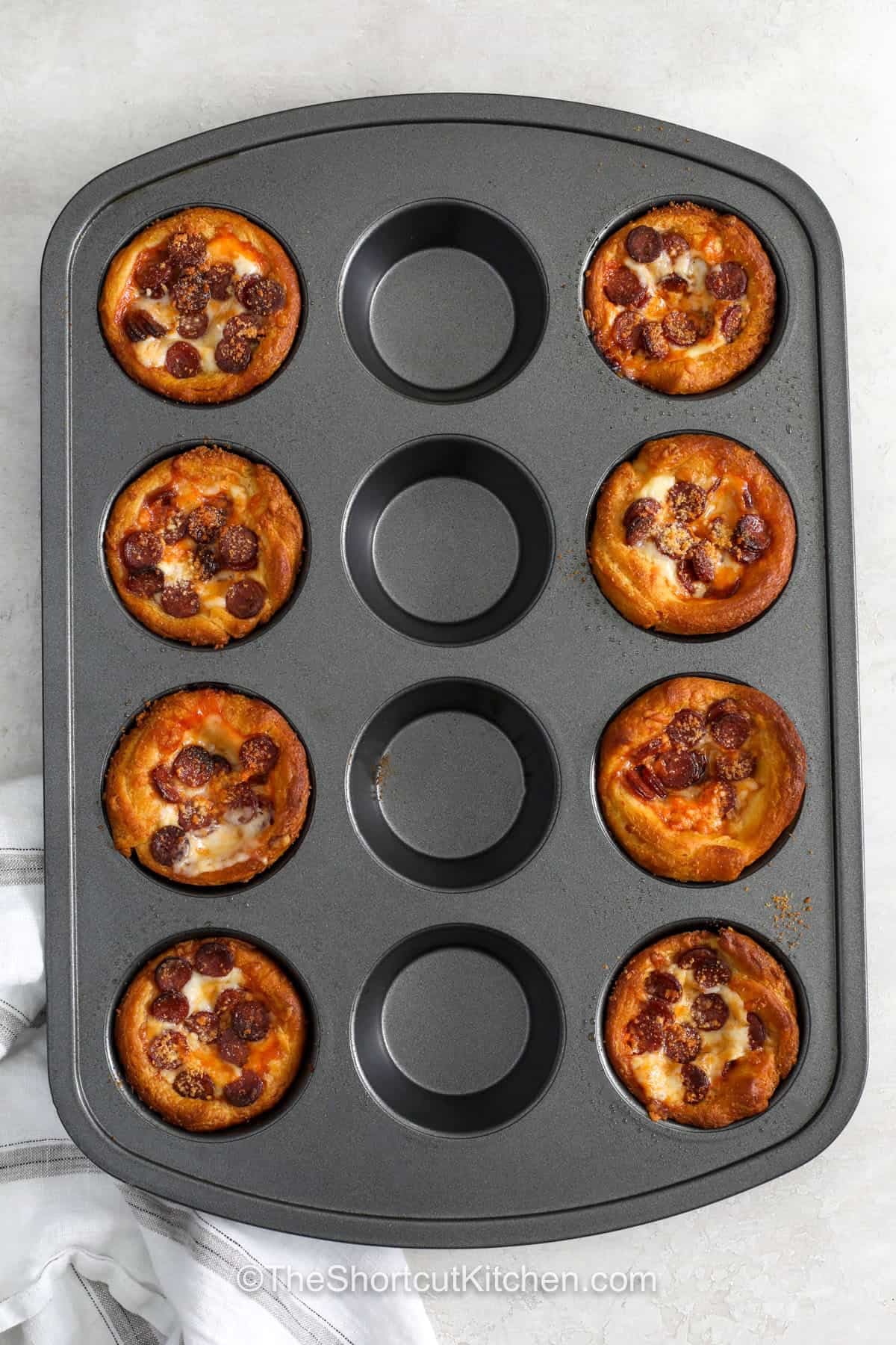 Pizza cupcakes are the answer when you want a fun snack with big pizza flavor. Flaky crescent roll dough wraps around pizza sauce, mozzarella, and mini pepperoni, while Parmesan adds an extra savory touch. These individual pizza bites are great for parties, game day, lunch, or an easy family treat. Change the toppings to please everyone at the table. Add this simple pizza cupcakes recipe to your menu. #theshortcutkitchen Pizza Cupcakes in the muffin tin.