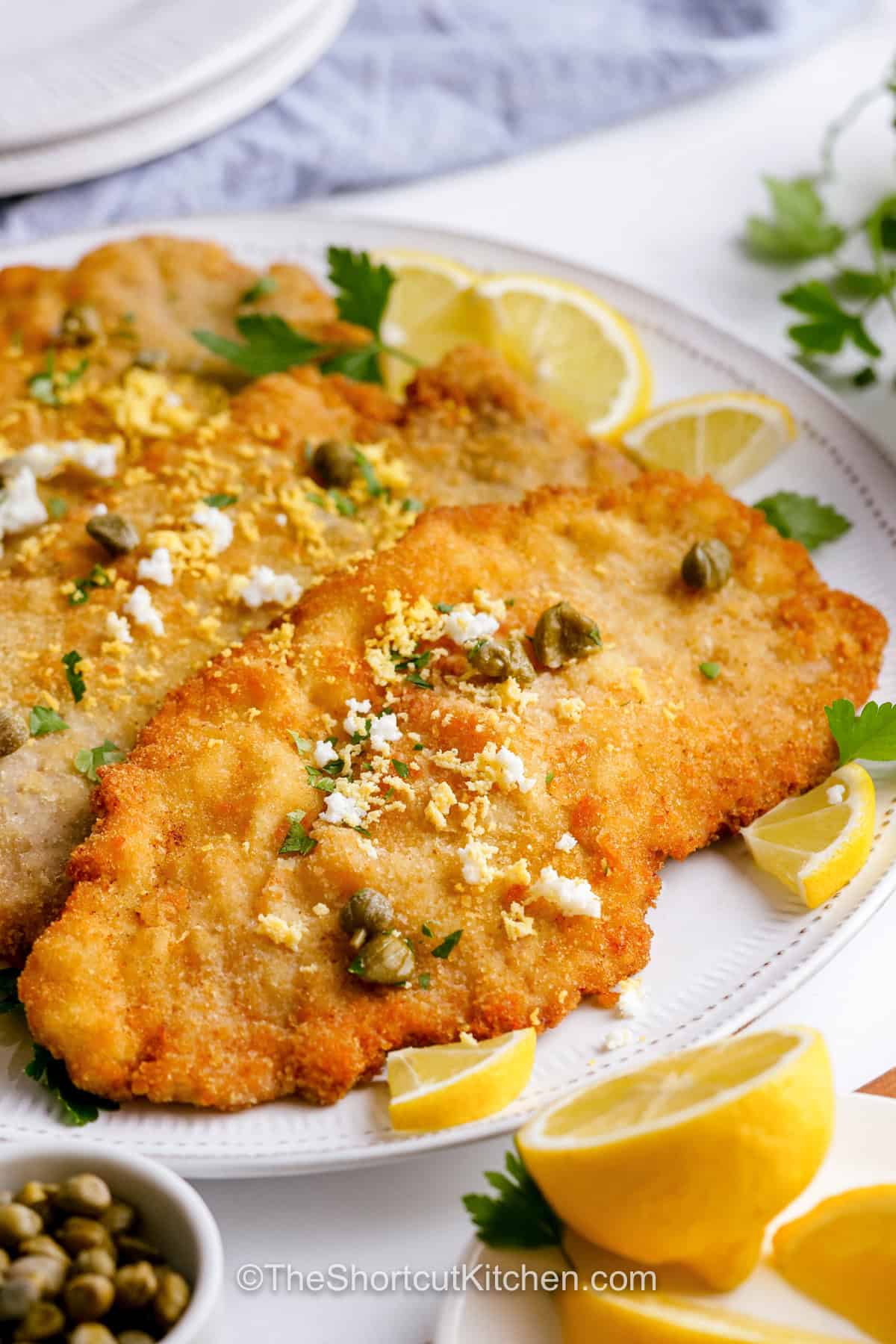 Make this crispy pork schnitzel recipe at home with tender pork tenderloin, simple breadcrumbs, and a hot skillet. This Pork Schnitzel Recipe uses a classic breading method for an even golden crust while keeping the thin pork cutlets tender and juicy. Lemon wedges and capers balance the rich, crunchy coating with bright flavor. It's an easy pork dinner that cooks quickly. Save this simple schnitzel recipe now. #theshortcutkitchen Pork Schnitzel Recipe on a plate.